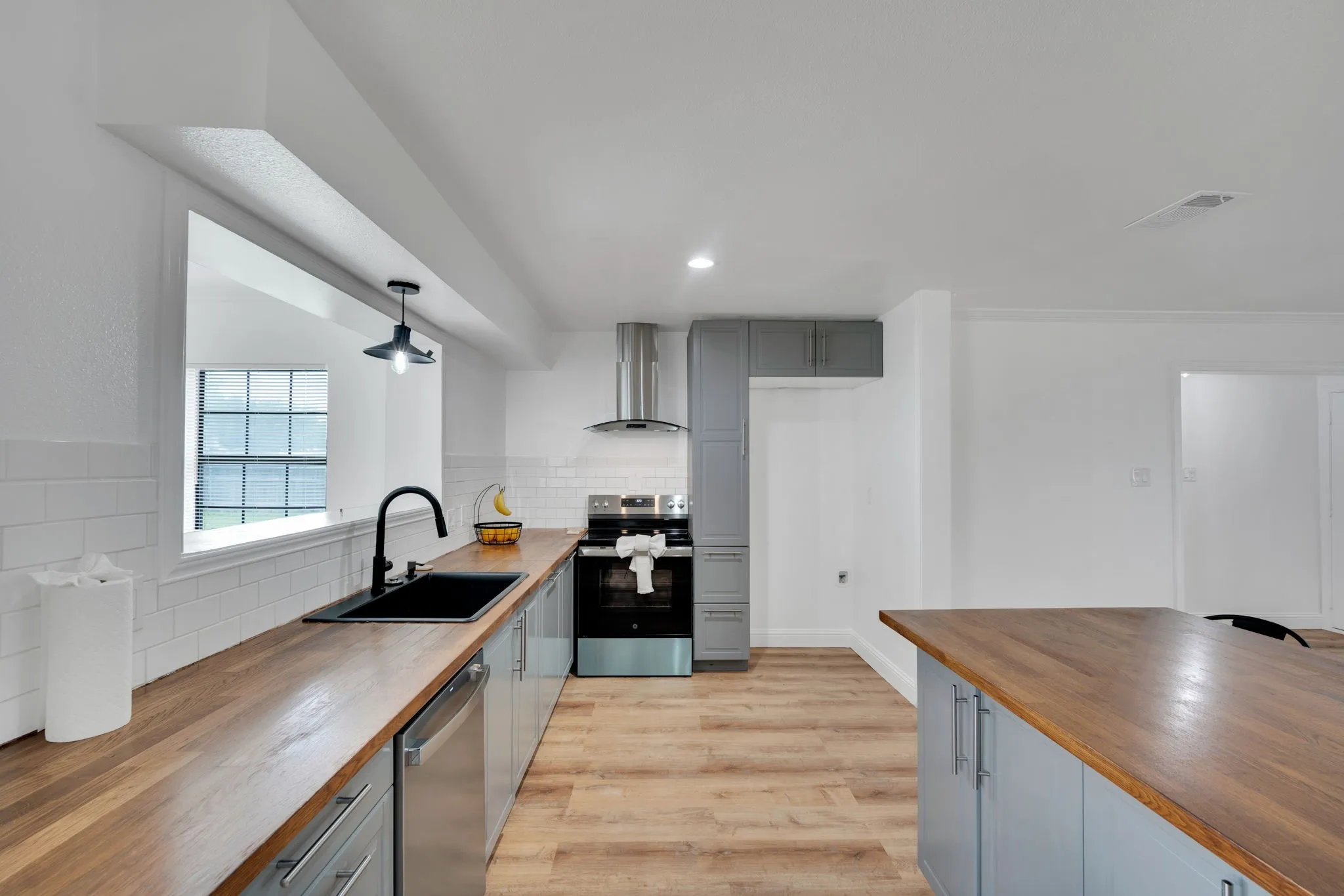Kitchen featuring butcher block countertops, gray cabinetry, stainless steel appliances, white subway tile backsplash, and wood-finish flooring