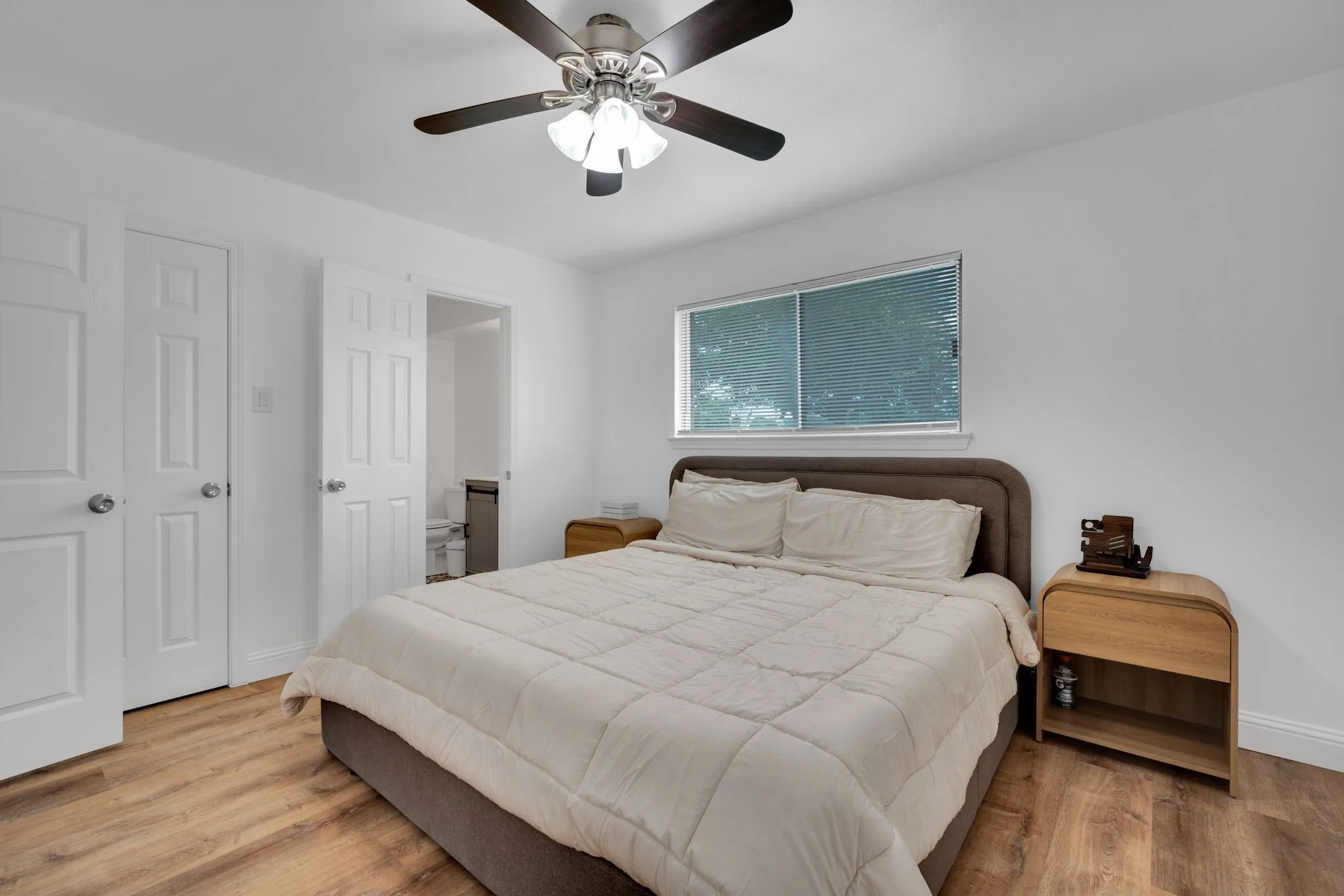 Bright bedroom featuring wood-finish flooring, a ceiling fan with integrated lighting, and multiple panel doors