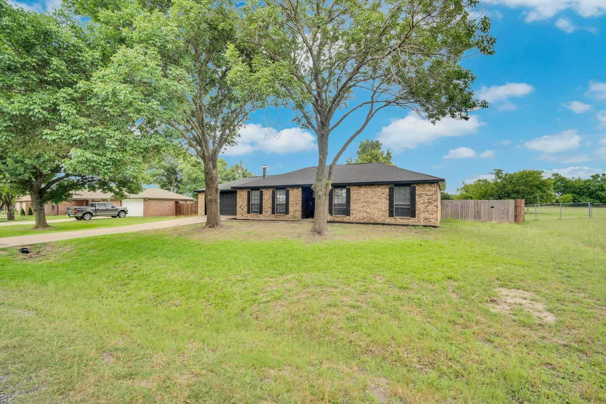 Ranch-style residence featuring a brick facade, dark roofing, and black window shutters