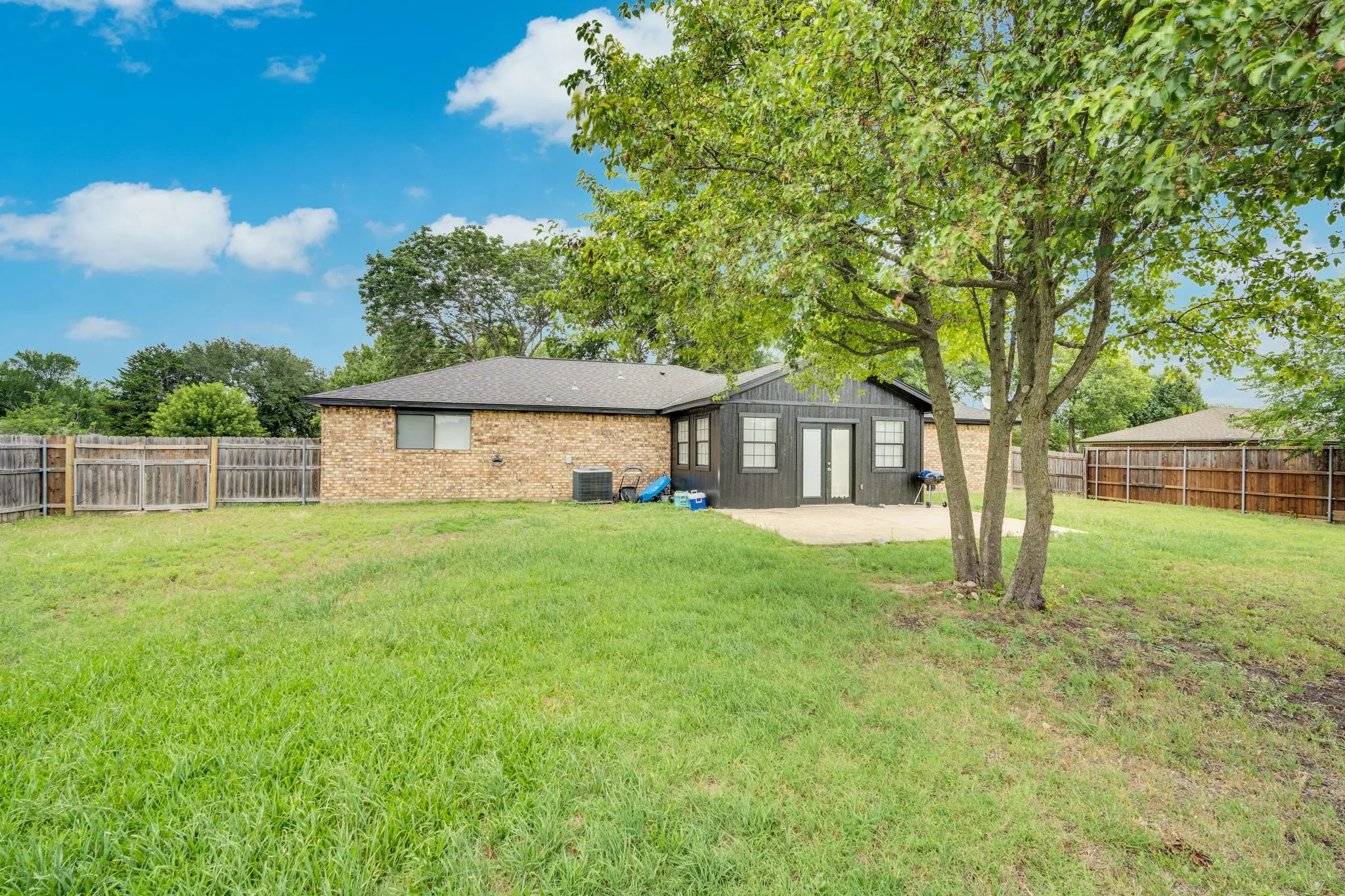 Expansive backyard featuring a large grass area, mature trees, and a concrete patio