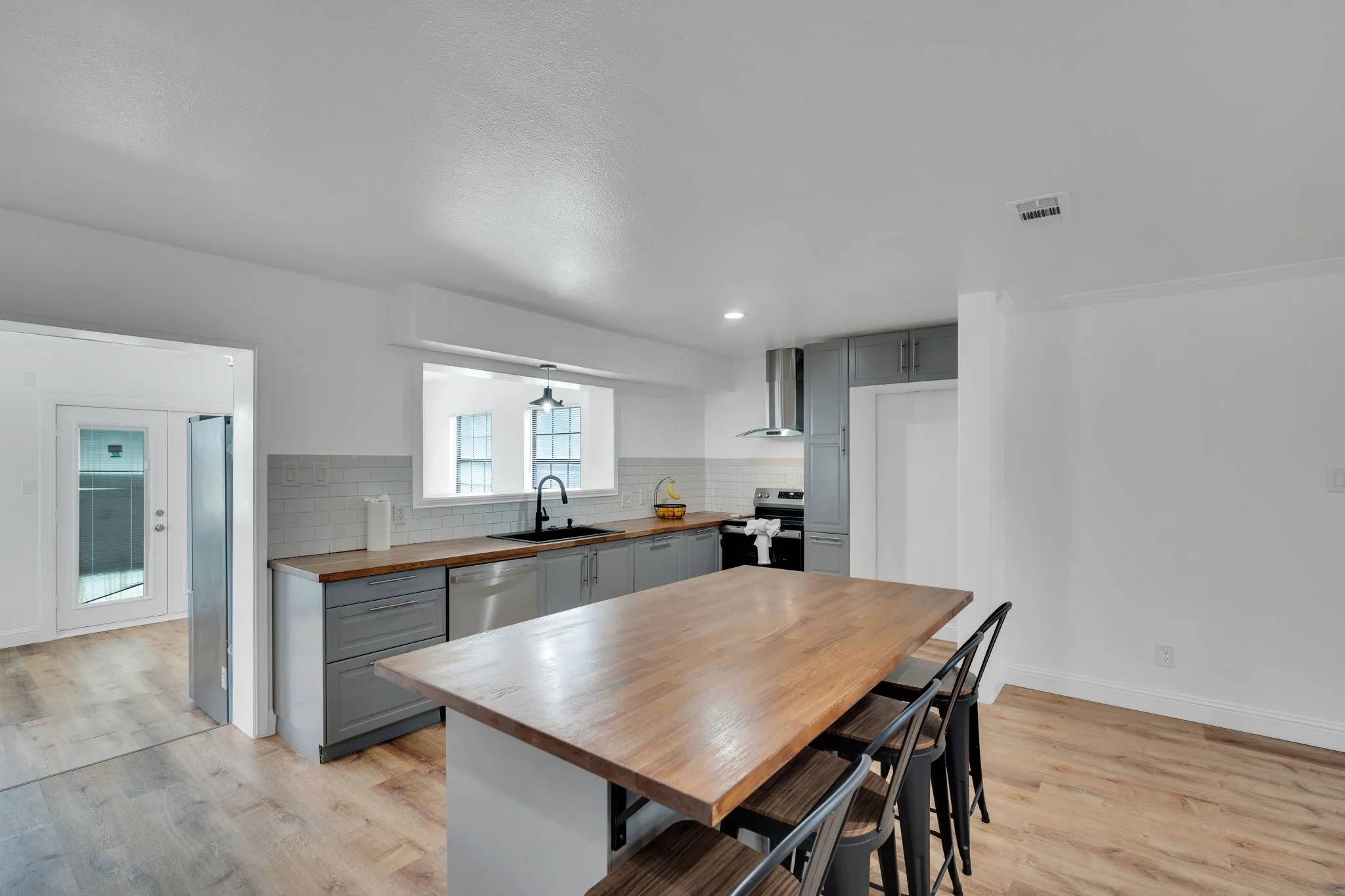 Modern kitchen featuring a large wood-finish island with seating, gray cabinetry, stainless steel appliances, and wood-finish flooring