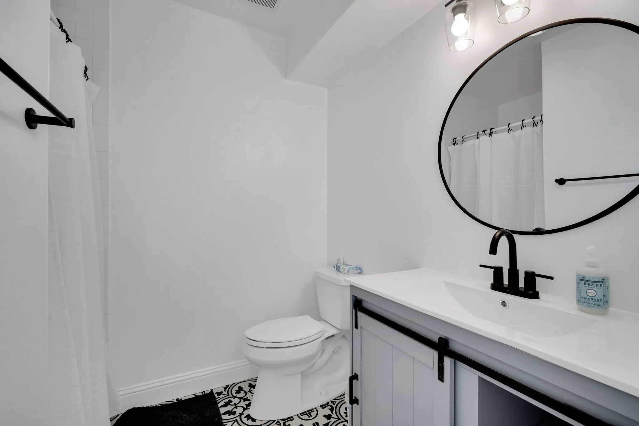 Bathroom featuring a vanity with a white countertop and undermount sink, matte black faucet, and a round mirror