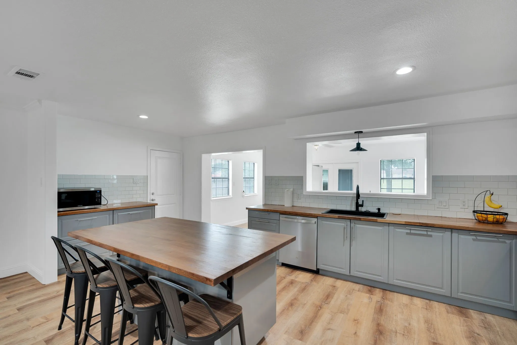 Contemporary kitchen featuring a spacious wood-finish island, light gray cabinetry, wood countertops, and subway tile backsplash