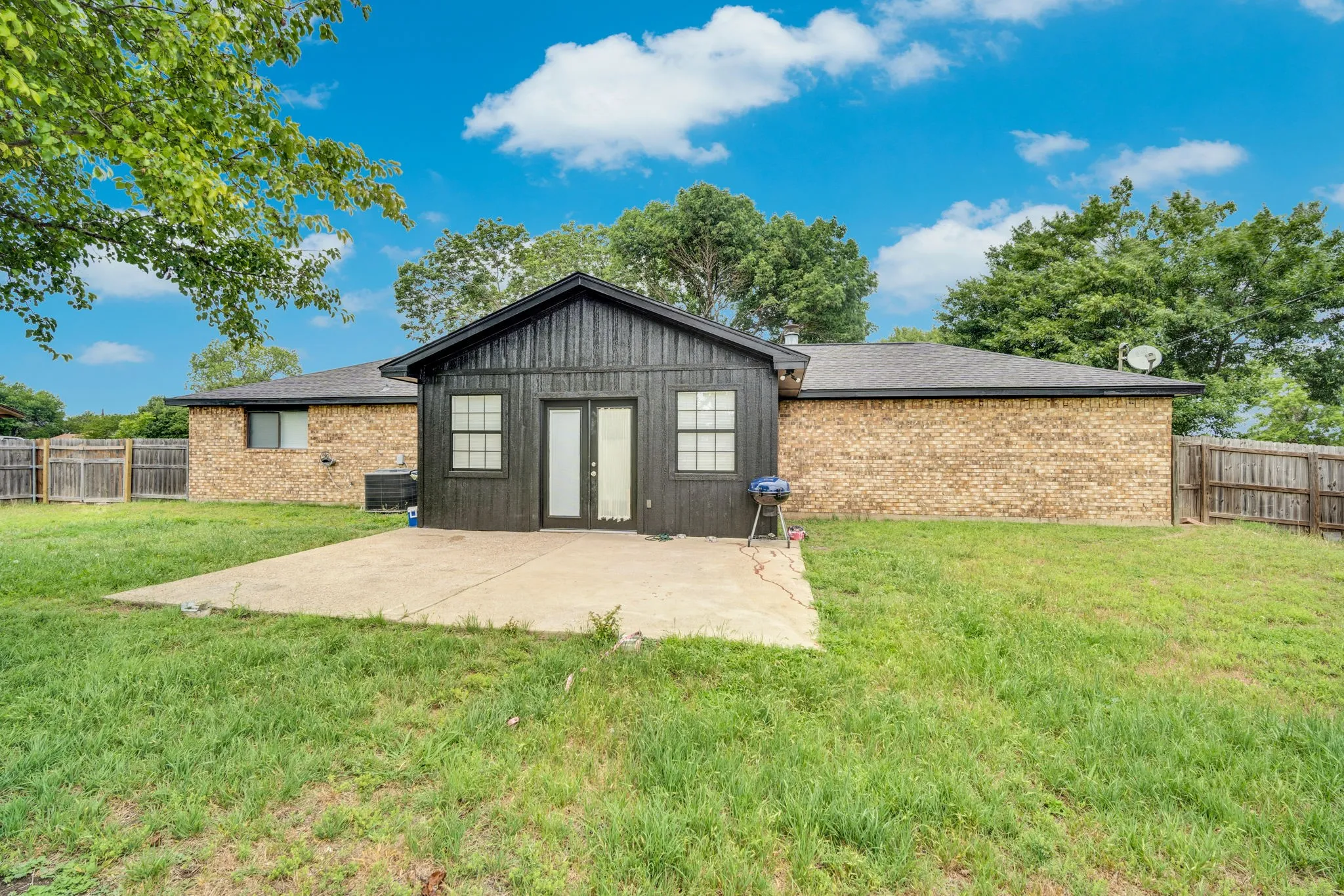 Spacious backyard featuring a concrete patio, a privacy fence, and mature trees