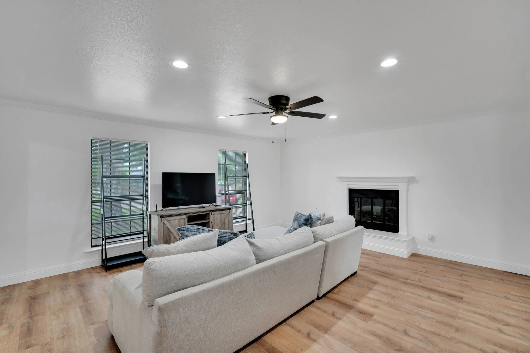 Living area featuring wood-finish flooring, a ceiling fan with integrated lighting, recessed ceiling lights, and crown molding
