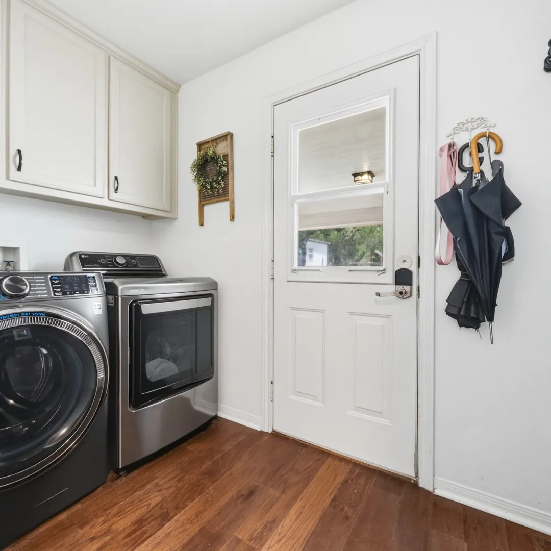 Laundry area featuring wood-finish flooring and white cabinetry with dark hardware