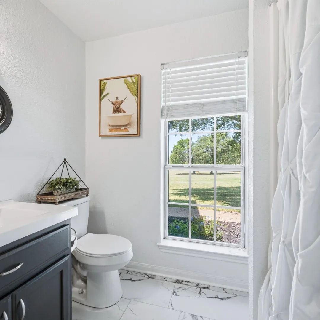 Bright bathroom featuring a white toilet, black vanity with a white countertop, and white flooring with dark veining