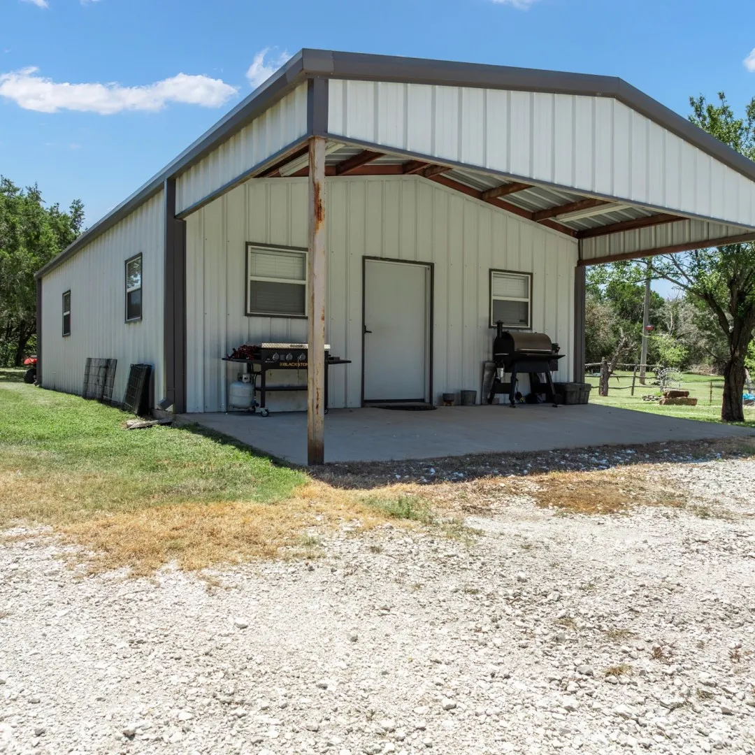 Metal-sided building featuring a covered concrete patio and a gravel approach