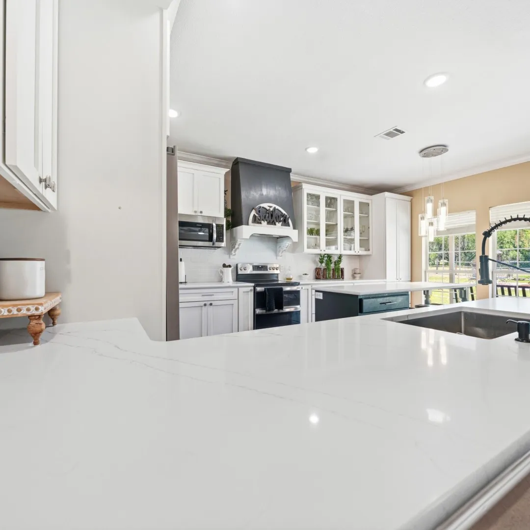 Kitchen featuring white cabinetry, light-toned countertops, a built-in range, a black range hood, and an undermount sink with a gooseneck faucet