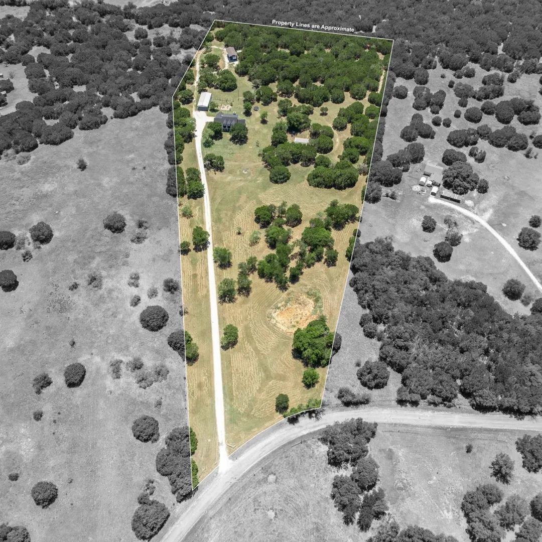 Expansive rural property featuring a long gravel driveway, a main residence, a secondary structure, abundant mature trees, and open land
