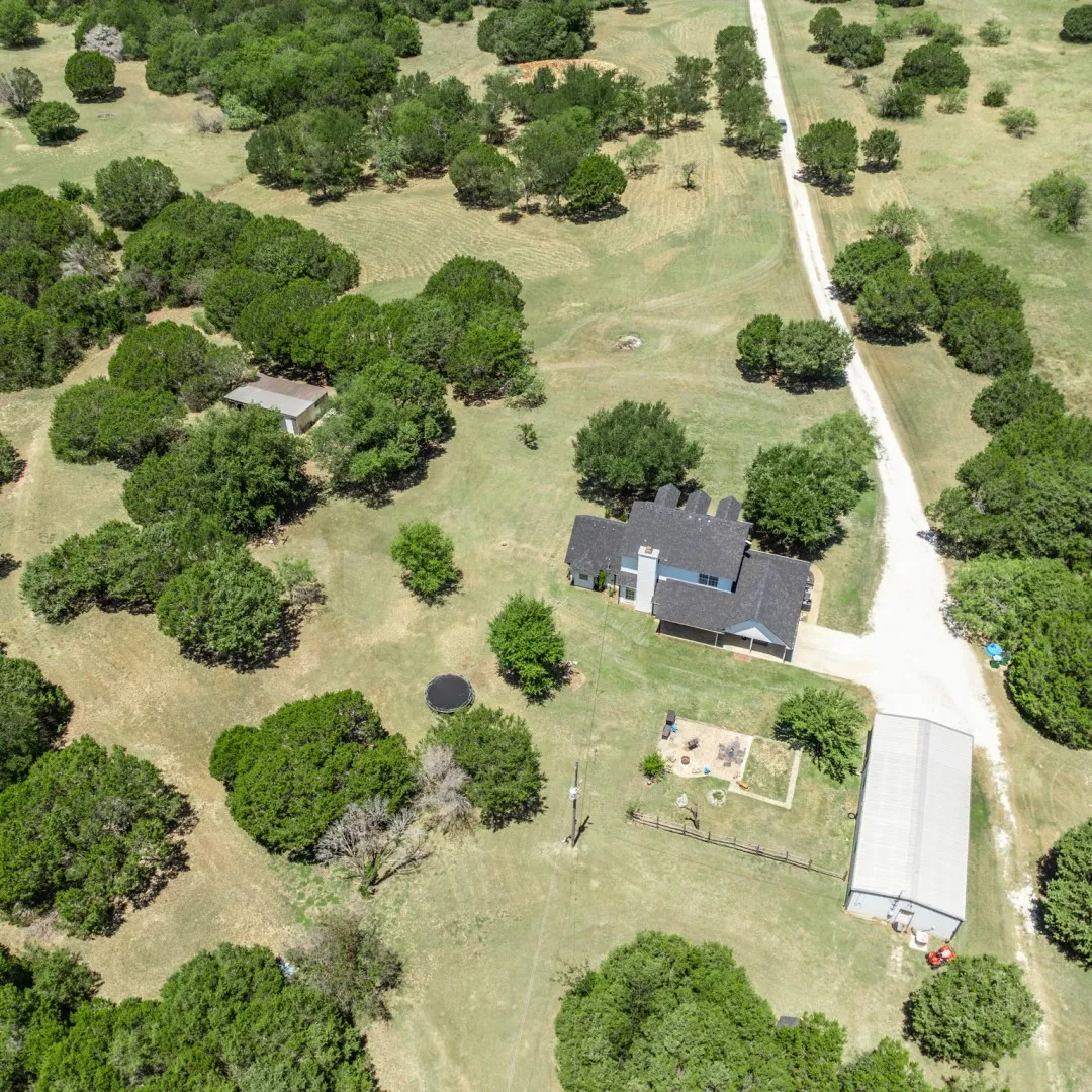 Aerial perspective showcasing a sprawling property featuring a two-story residence, extensive green space, a metal outbuilding, and a gravel driveway