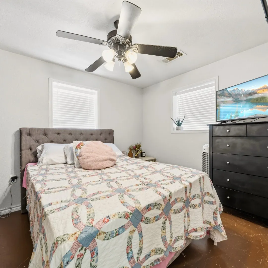 Neutral wall paint with two windows featuring blinds, a ceiling fan with integrated lighting, and dark-toned flooring