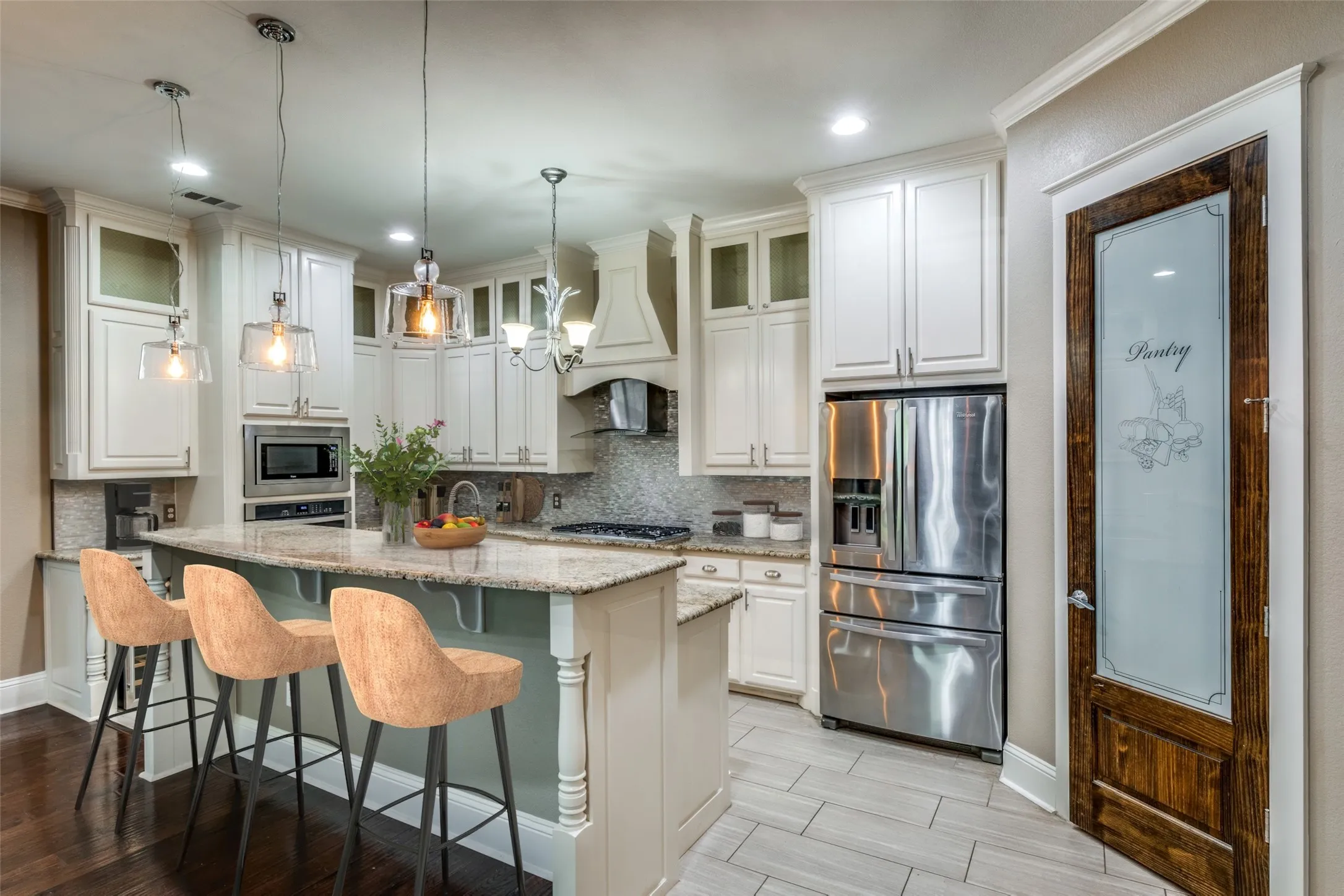 Kitchen featuring a large island with stone countertop, white cabinetry with glass upper doors, stainless steel appliances, and a decorative pantry door with frosted glass