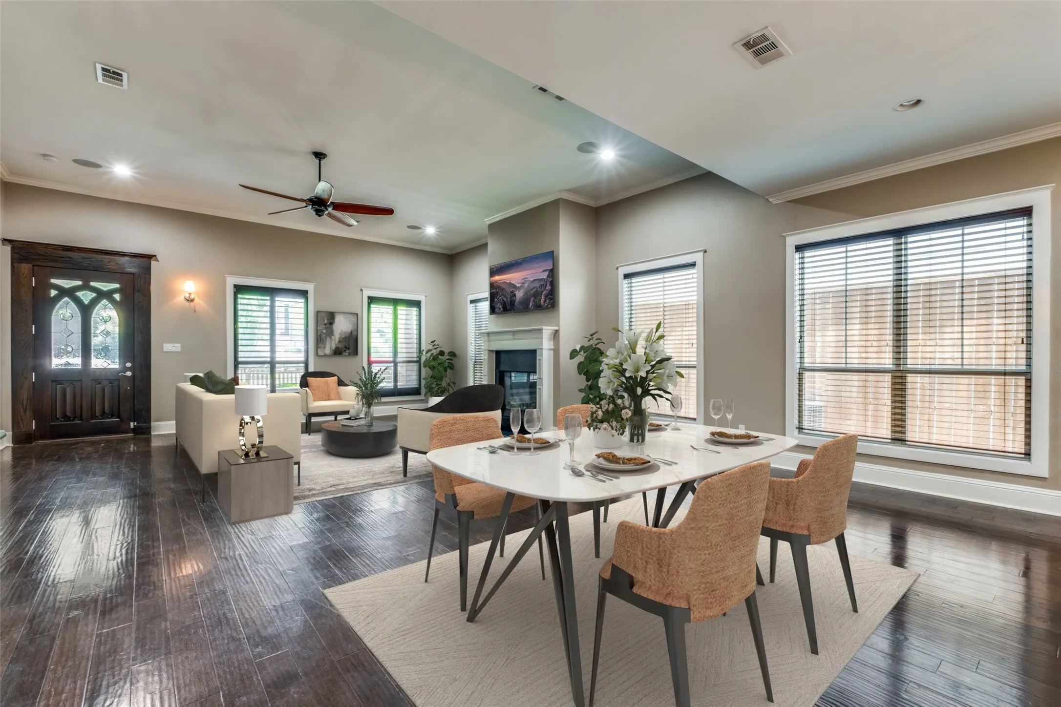 Open-concept living and dining areas featuring dark wood-finish flooring, a decorative front entry door, recessed lighting, and multiple windows with blinds