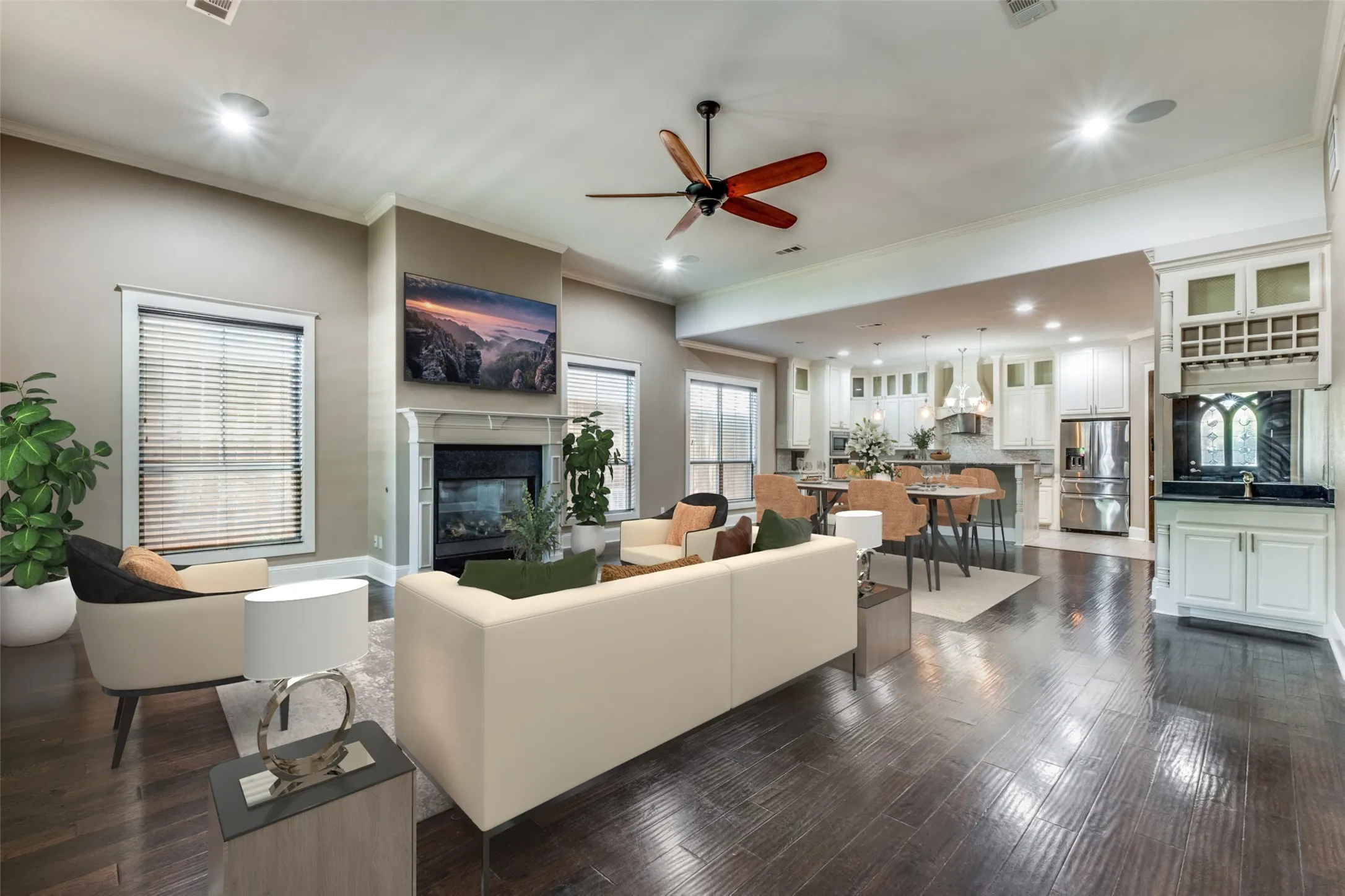Open-concept living space featuring wood-finish flooring, a fireplace with a mantel, and a kitchen with white cabinetry