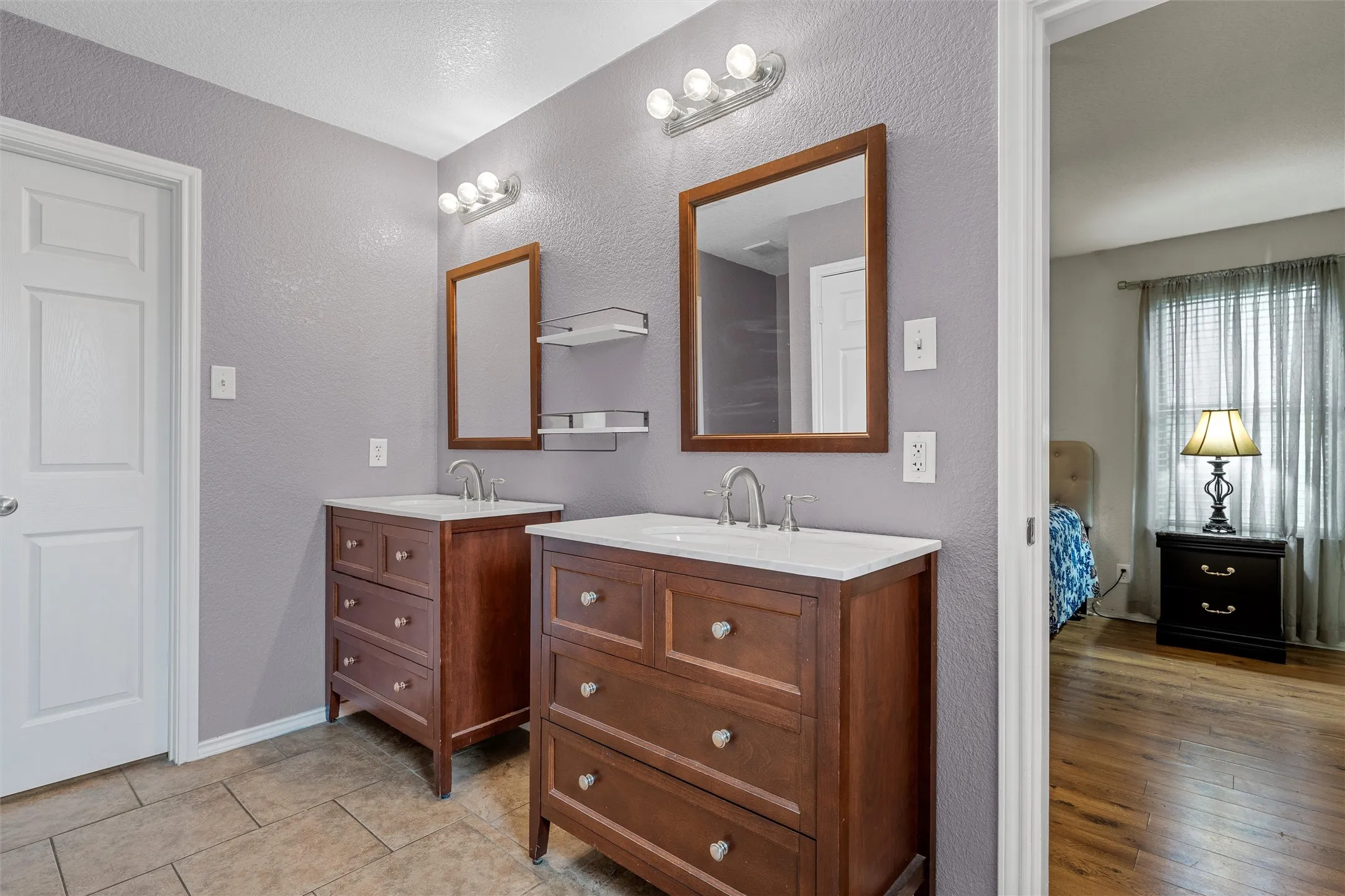 Dual wood-finish vanities with integrated sinks, framed mirrors, and overhead vanity lighting