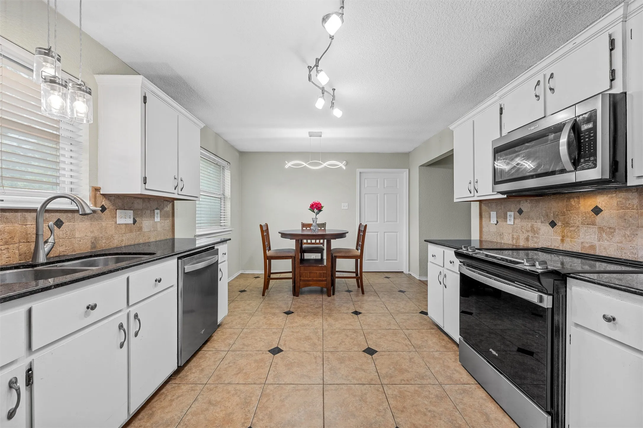 Kitchen featuring white cabinetry, dark countertops, a tile backsplash with accent inserts, and stainless steel appliances
