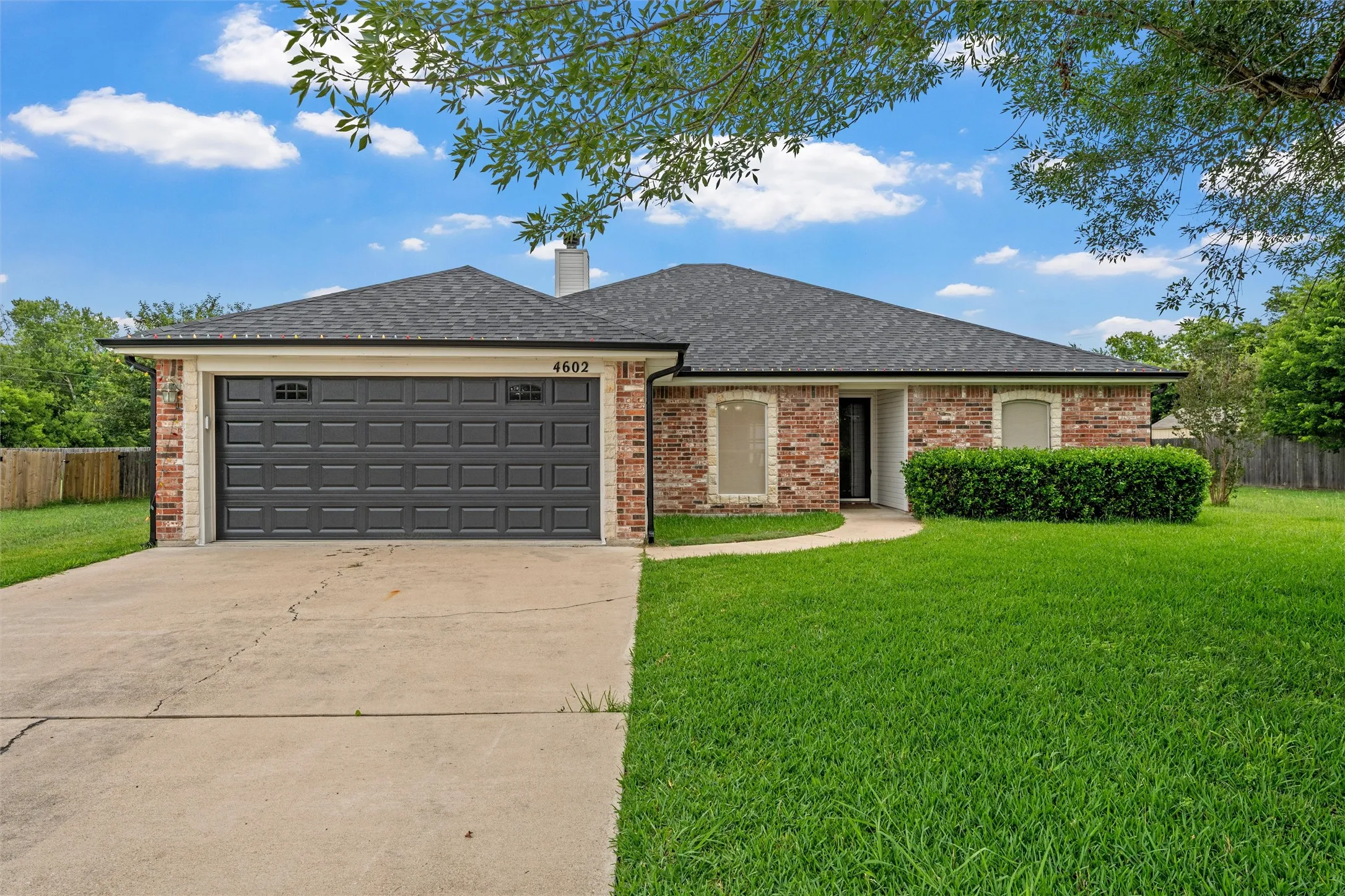 Brick facade residence featuring a dark gray garage door with decorative windows, a concrete driveway, a manicured lawn, and a curved sidewalk leading to the front entry