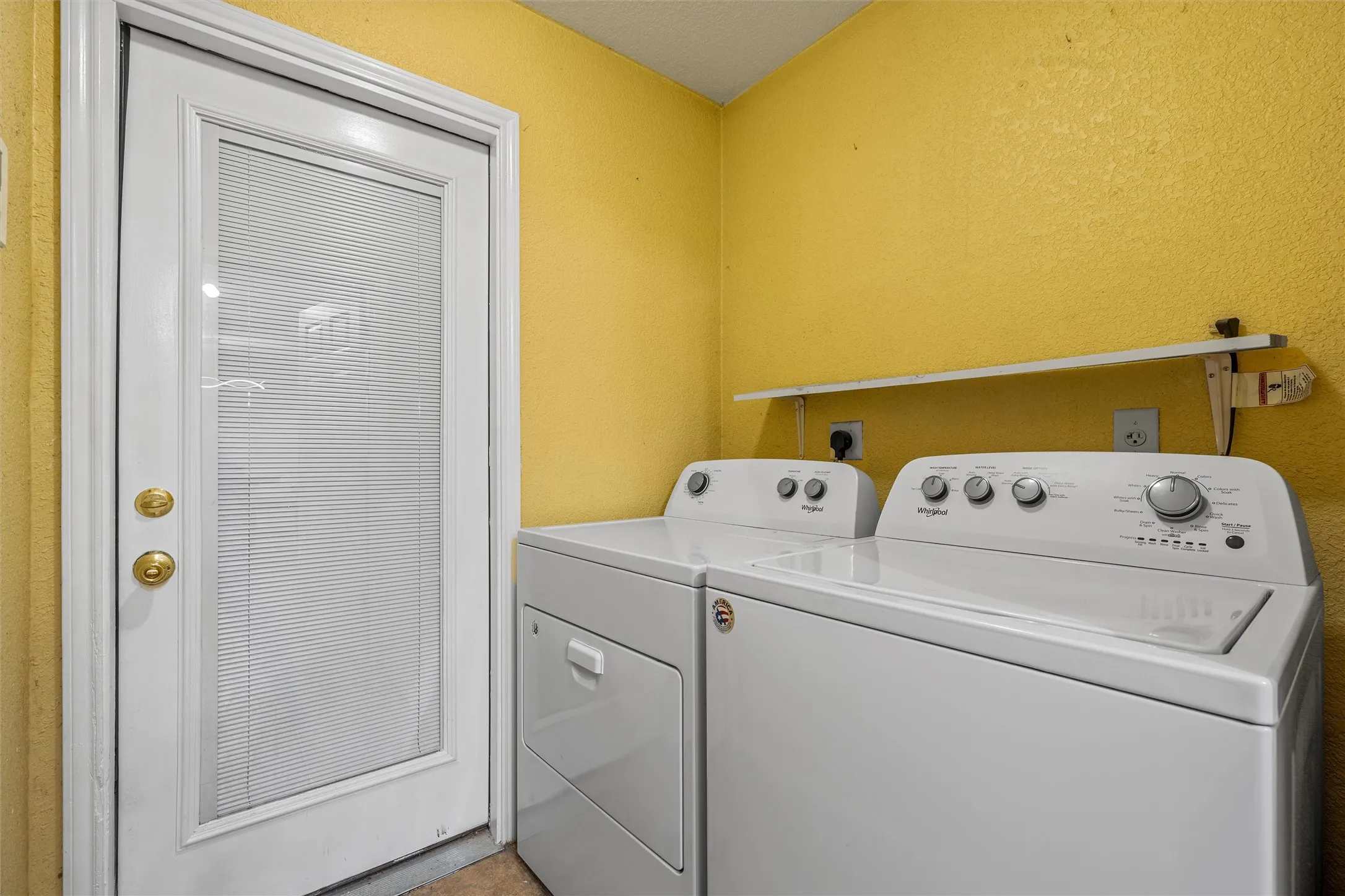 Dedicated utility space featuring a white door with internal blinds, brass hardware, and a built-in wall shelf