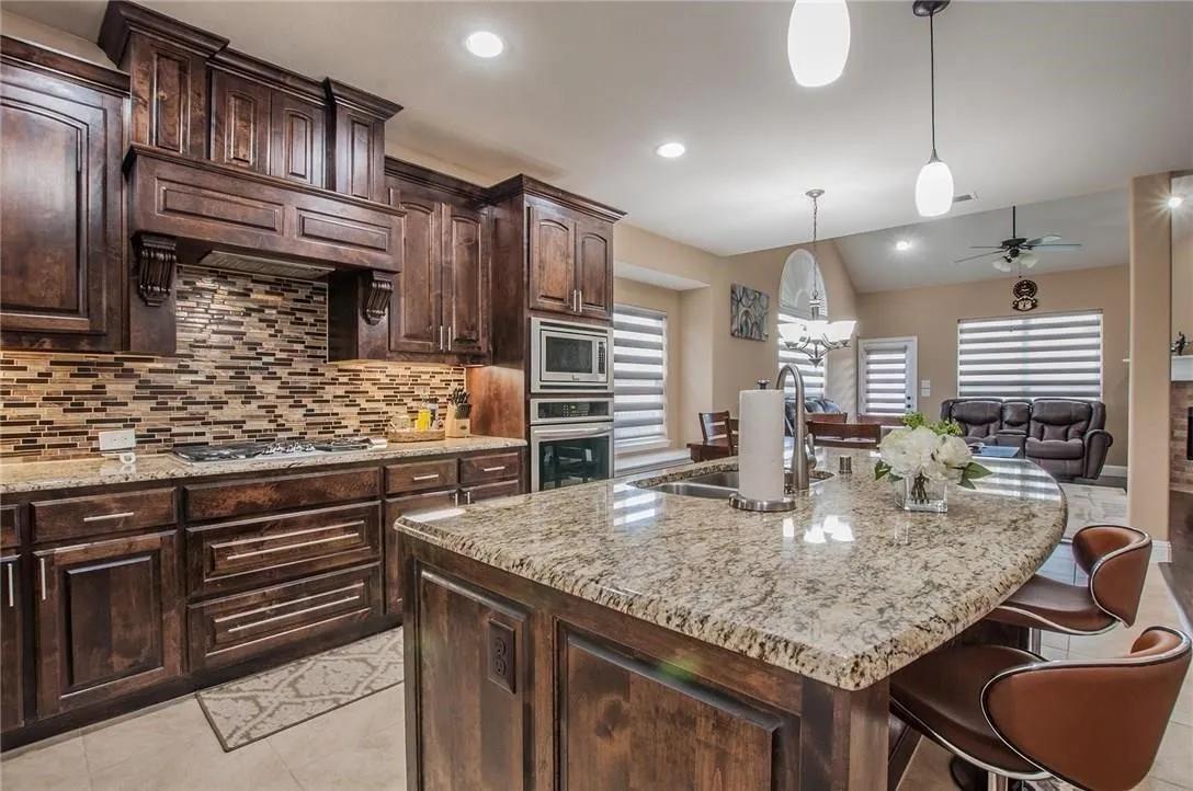 Gourmet kitchen featuring a granite island, dark wood cabinetry, built-in stainless steel appliances, a mosaic tile backsplash, and recessed lighting