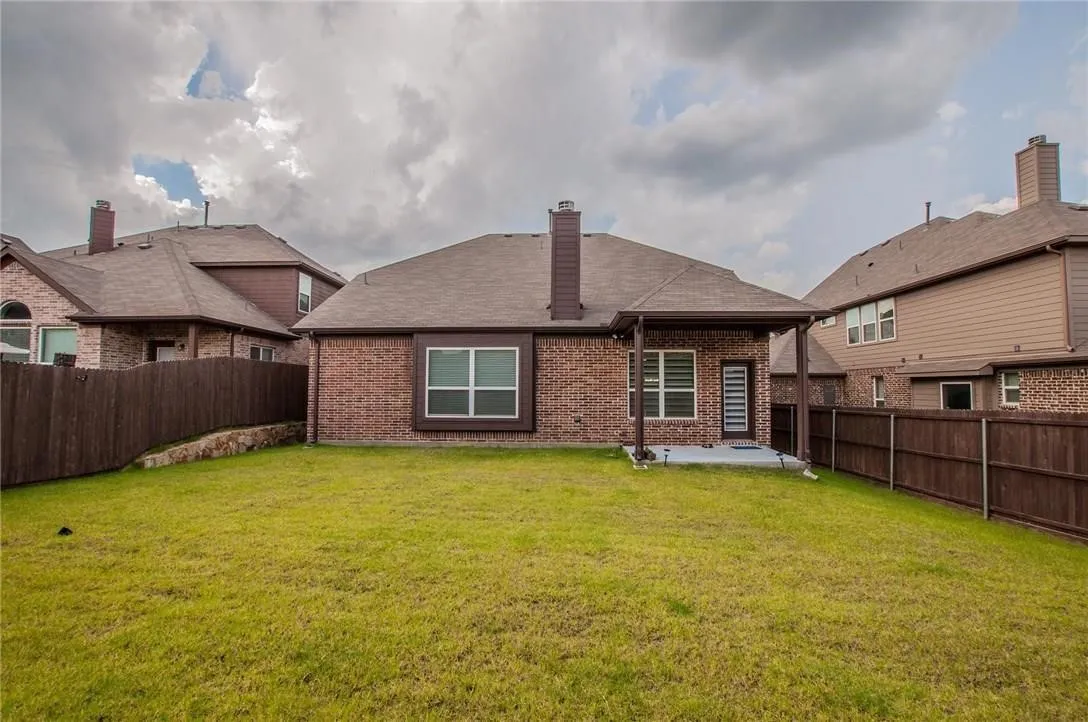 Expansive backyard featuring a manicured lawn, full privacy fencing, a covered patio, and a brick exterior