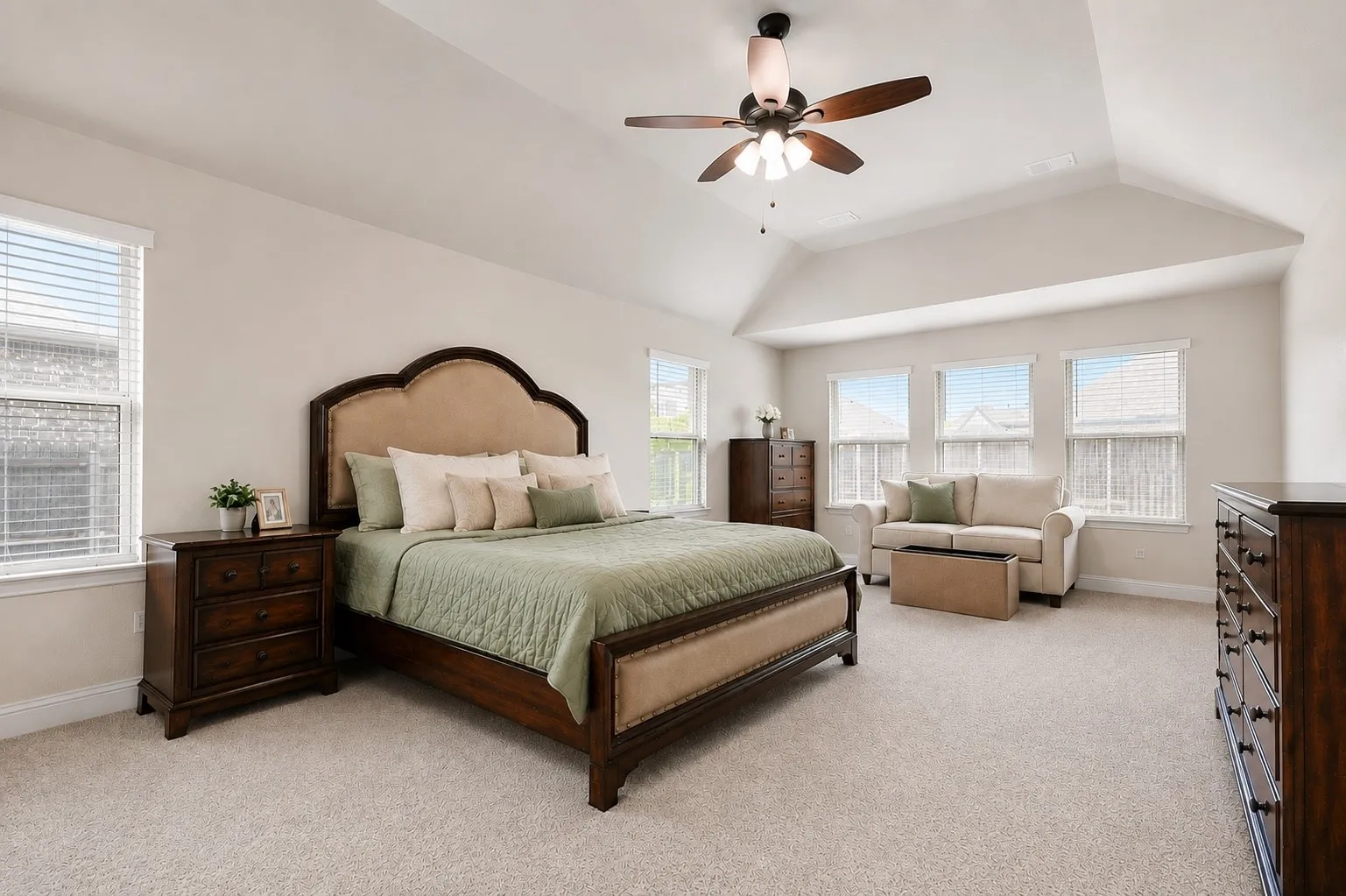 Spacious bedroom featuring vaulted ceilings, light-toned carpeting, multiple windows with blinds, and a ceiling fan with integrated lighting