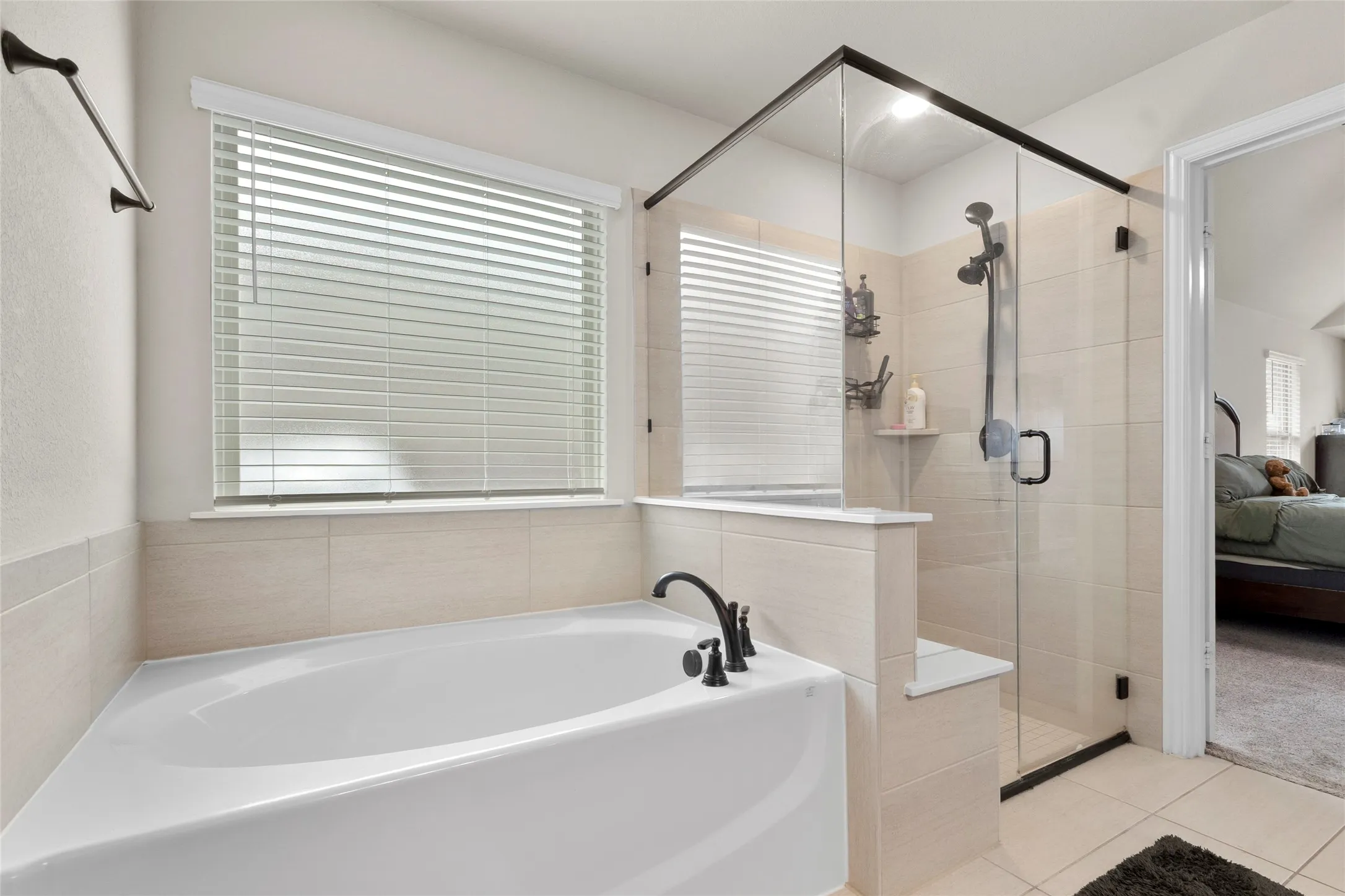 Soaking tub featuring a matte black faucet, surrounded by light-toned tile