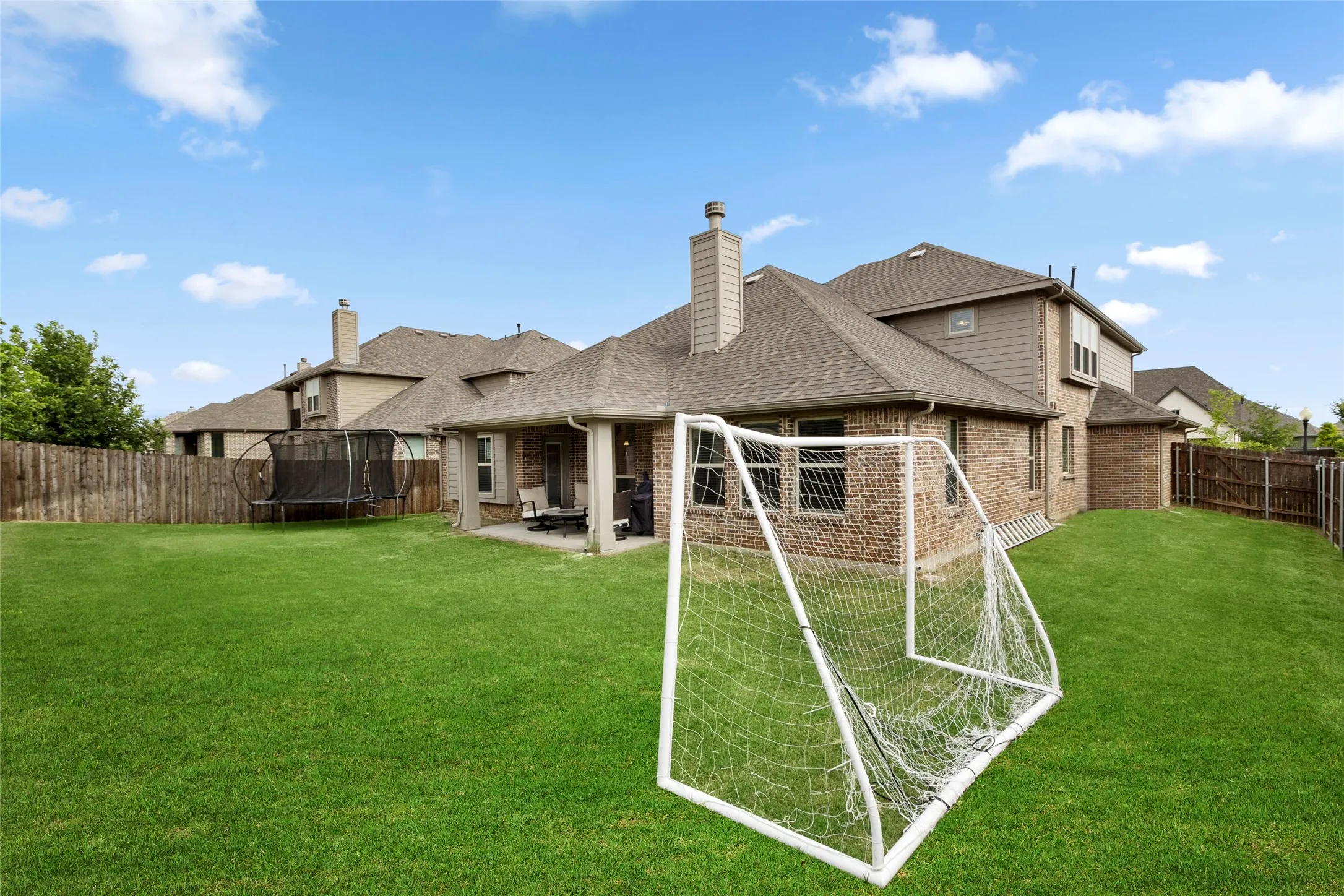 Expansive fenced backyard featuring a substantial lawn and covered patio area with concrete flooring