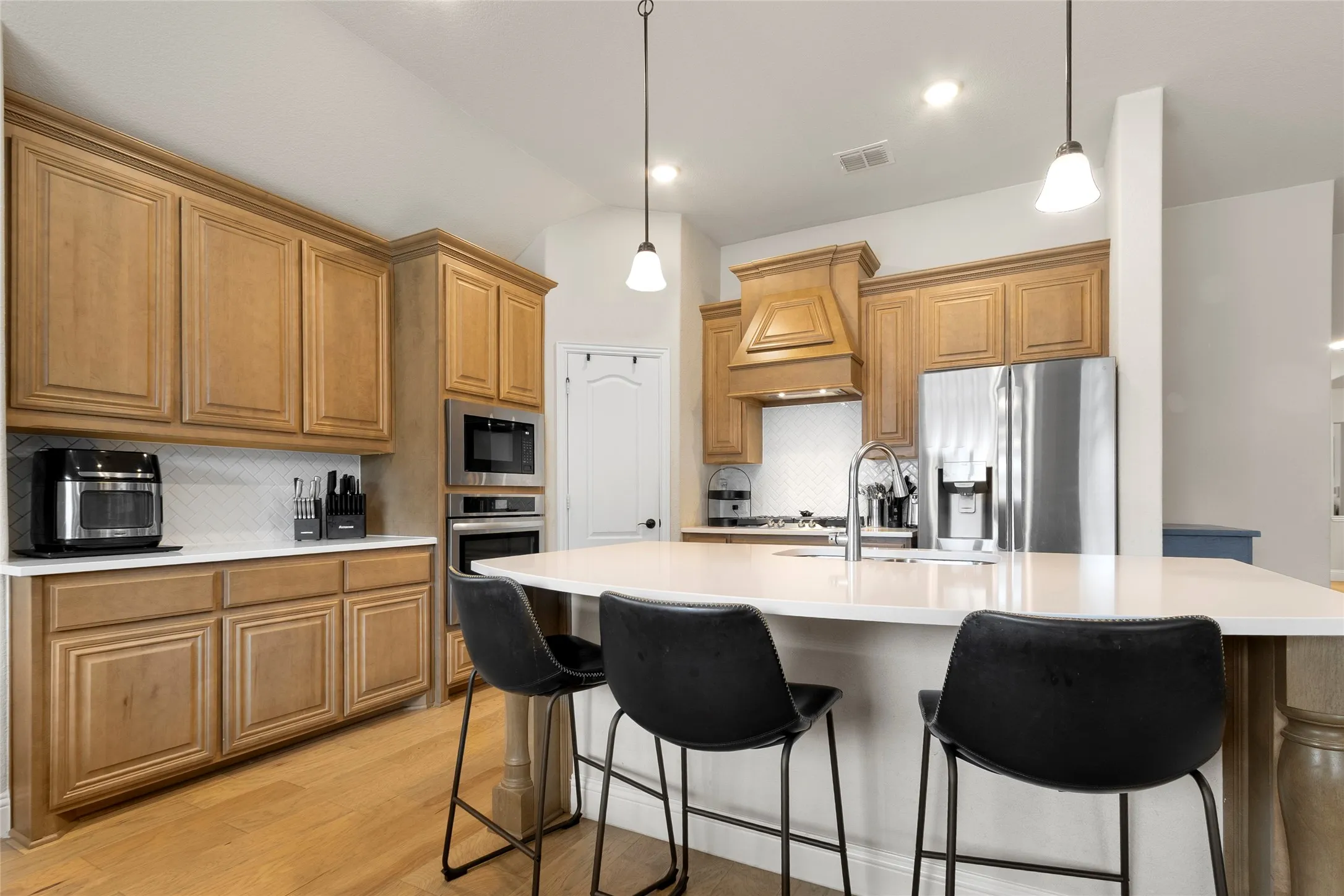 Gourmet kitchen featuring a large island with white countertop, rich wood cabinetry, stainless steel appliances, and a geometric tile backsplash