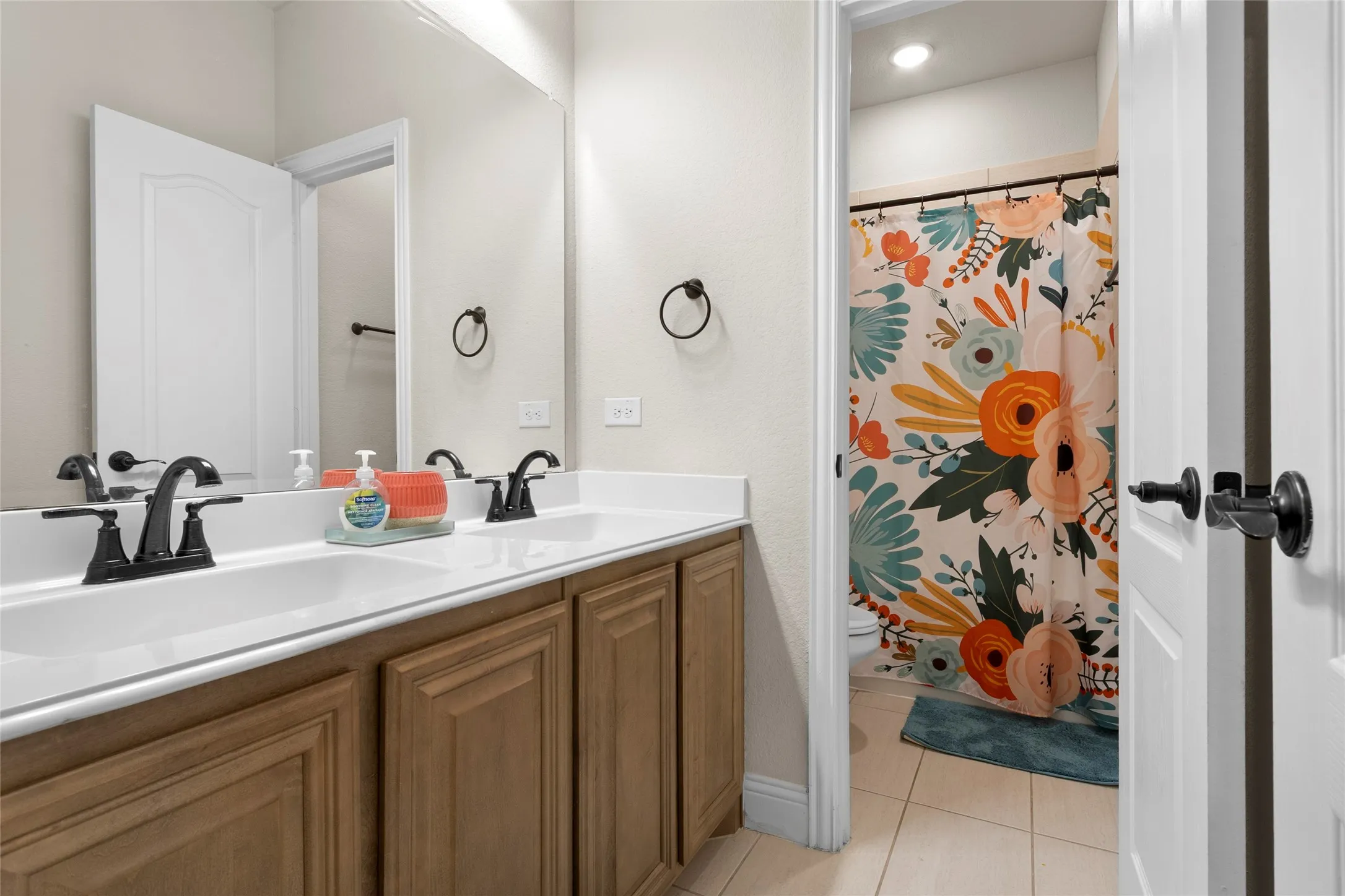 Dual vanity with matte black fixtures, white countertops, and wood-finish cabinetry