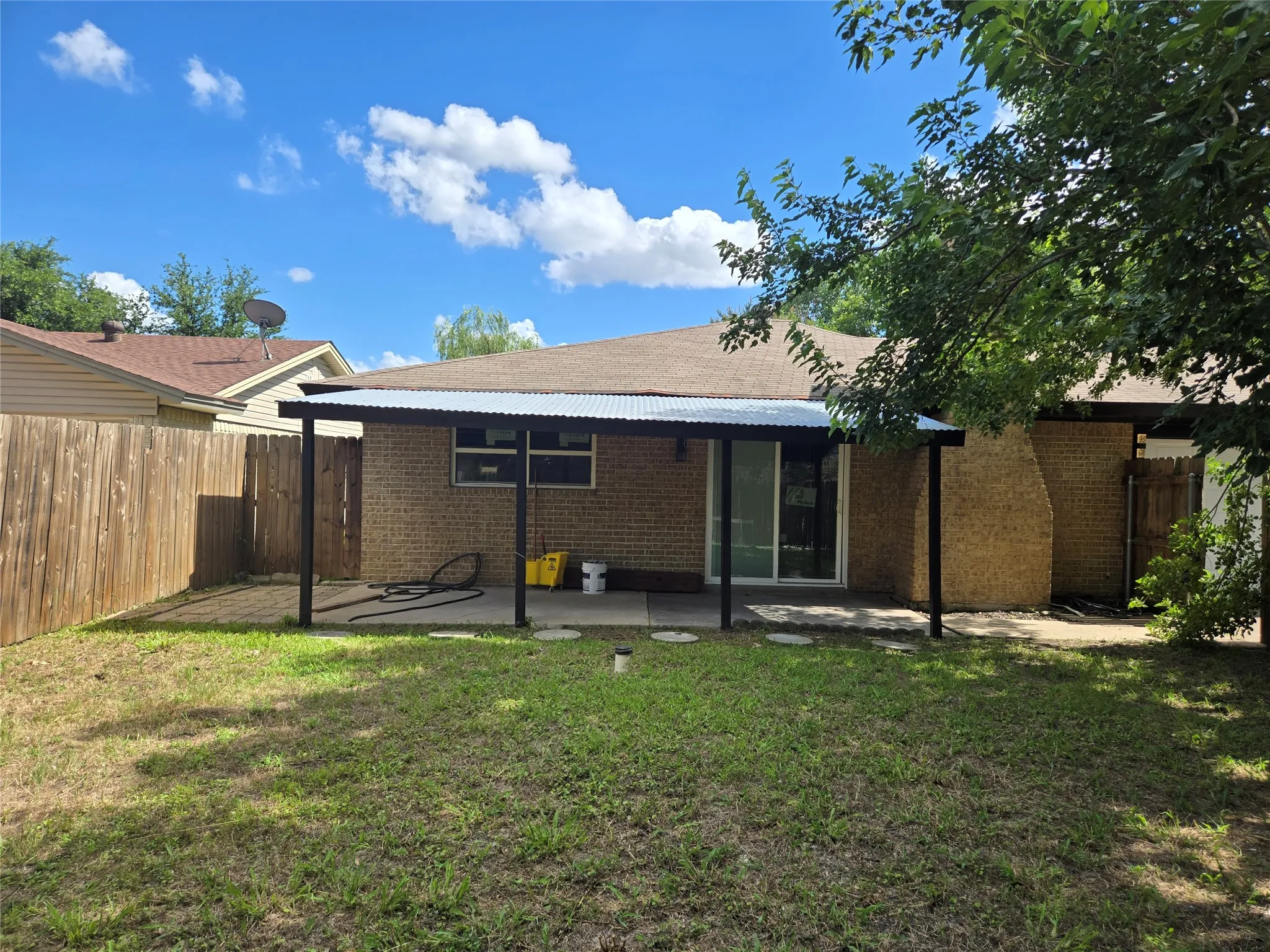 Brick exterior featuring a covered patio, sliding glass door, and a privacy fence