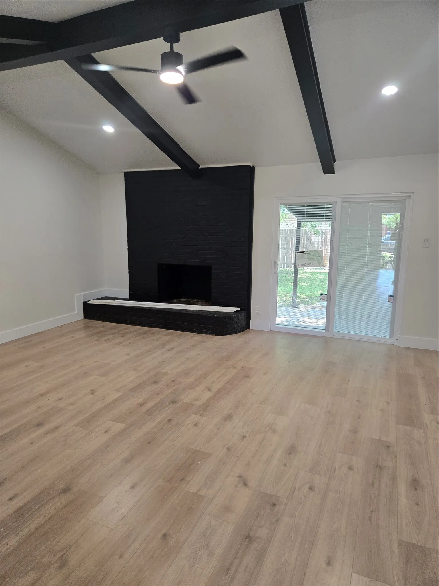 Modern living space featuring exposed beam ceiling detail with recessed lighting, ceiling fan, and wide-plank wood-finish flooring throughout