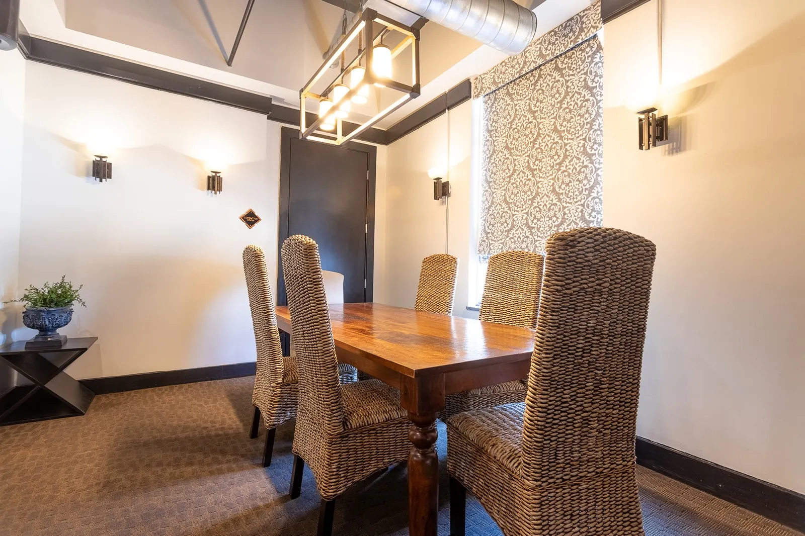 Dining area featuring a rectangular wood-finish table, patterned carpet flooring, and exposed ceiling ductwork