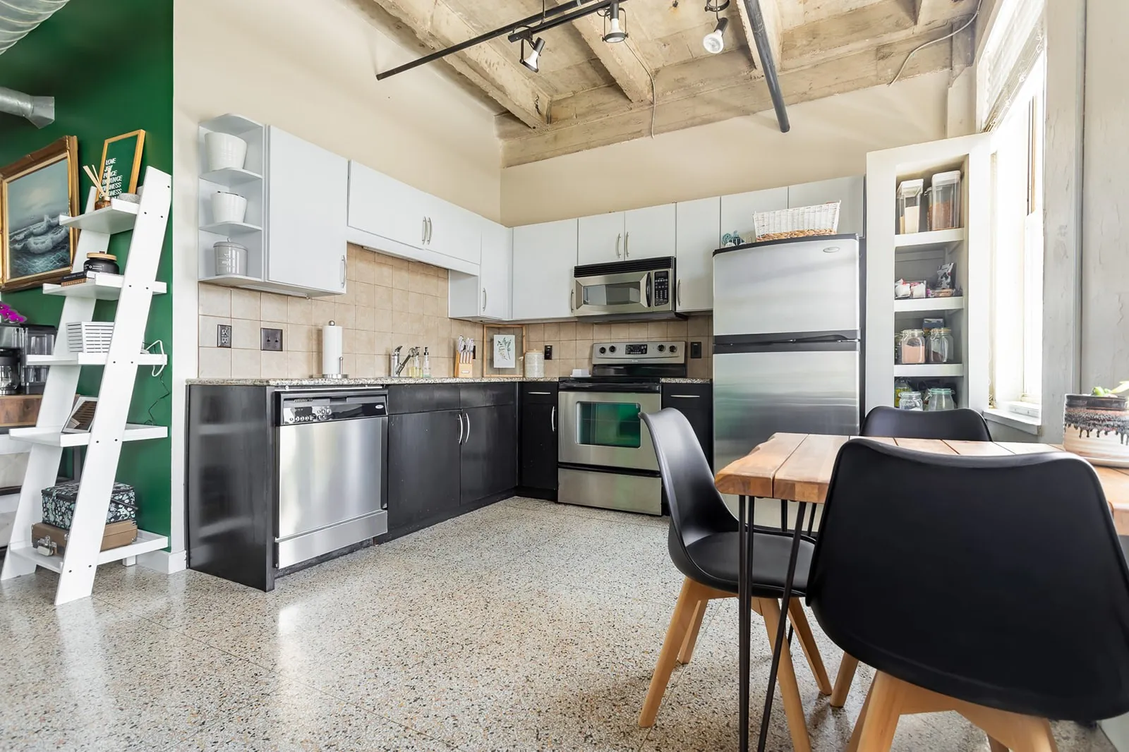 Kitchen featuring stainless steel appliances, concrete ceilings, light-colored backsplash, dark base cabinetry, and light upper cabinetry