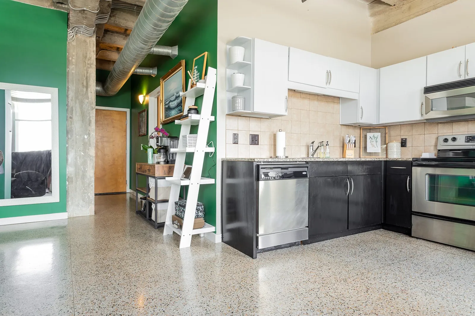 Open-concept kitchen featuring stainless steel appliances, dark base cabinetry, white upper cabinetry, and a light-colored tile backsplash
