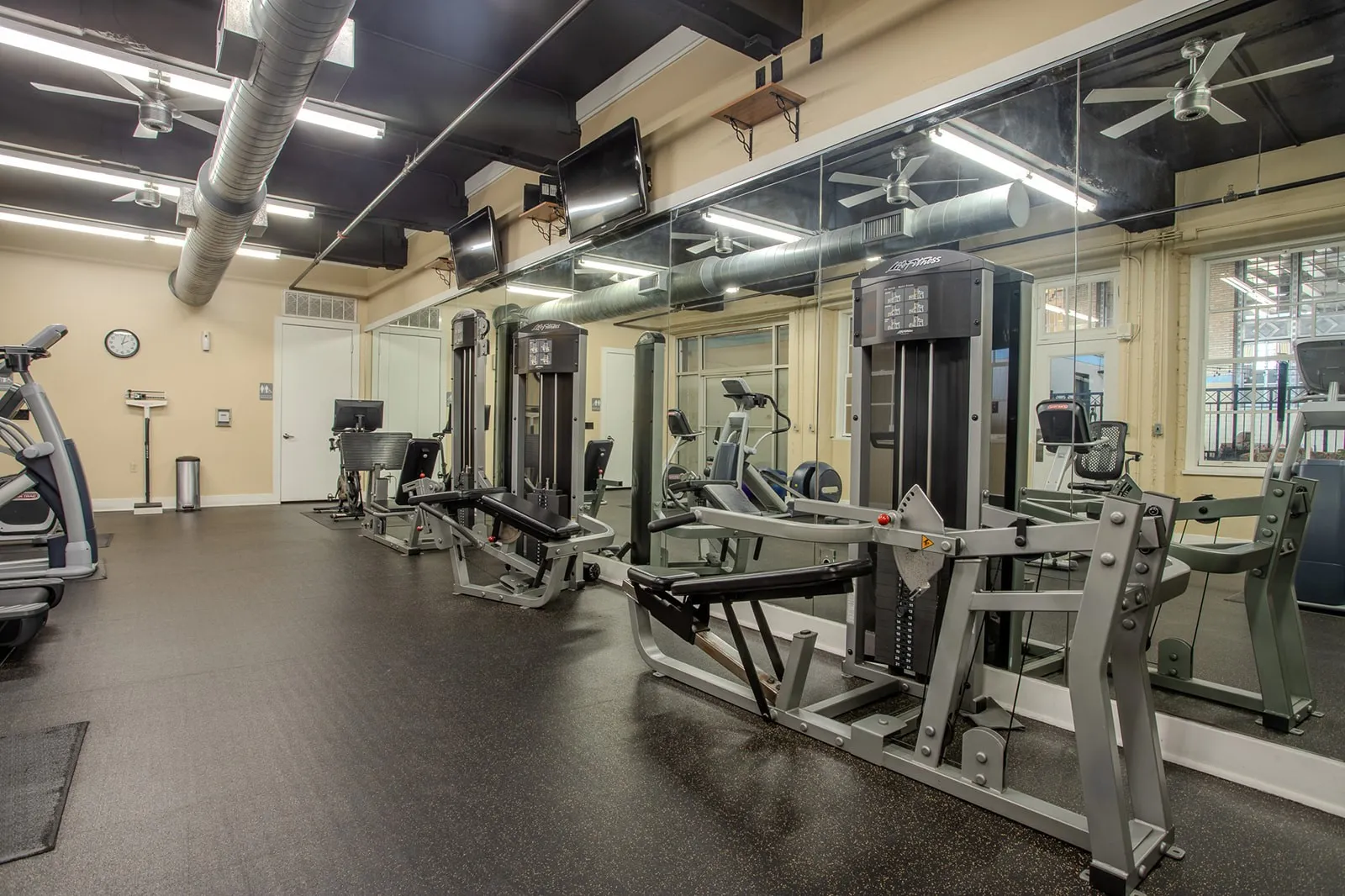 Fitness center featuring extensive mirrored walls, exposed industrial-style ductwork, recessed lighting, and multiple ceiling fans