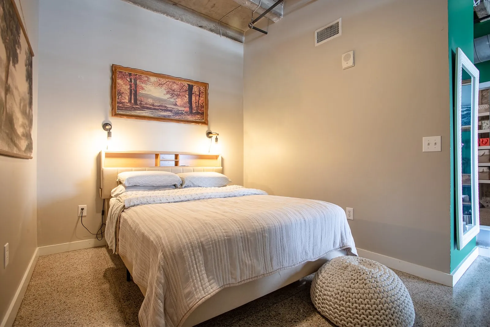 Bedroom featuring light gray walls, exposed concrete ceiling, built-in headboard lighting, recessed wall vent, and neutral-toned carpeting
