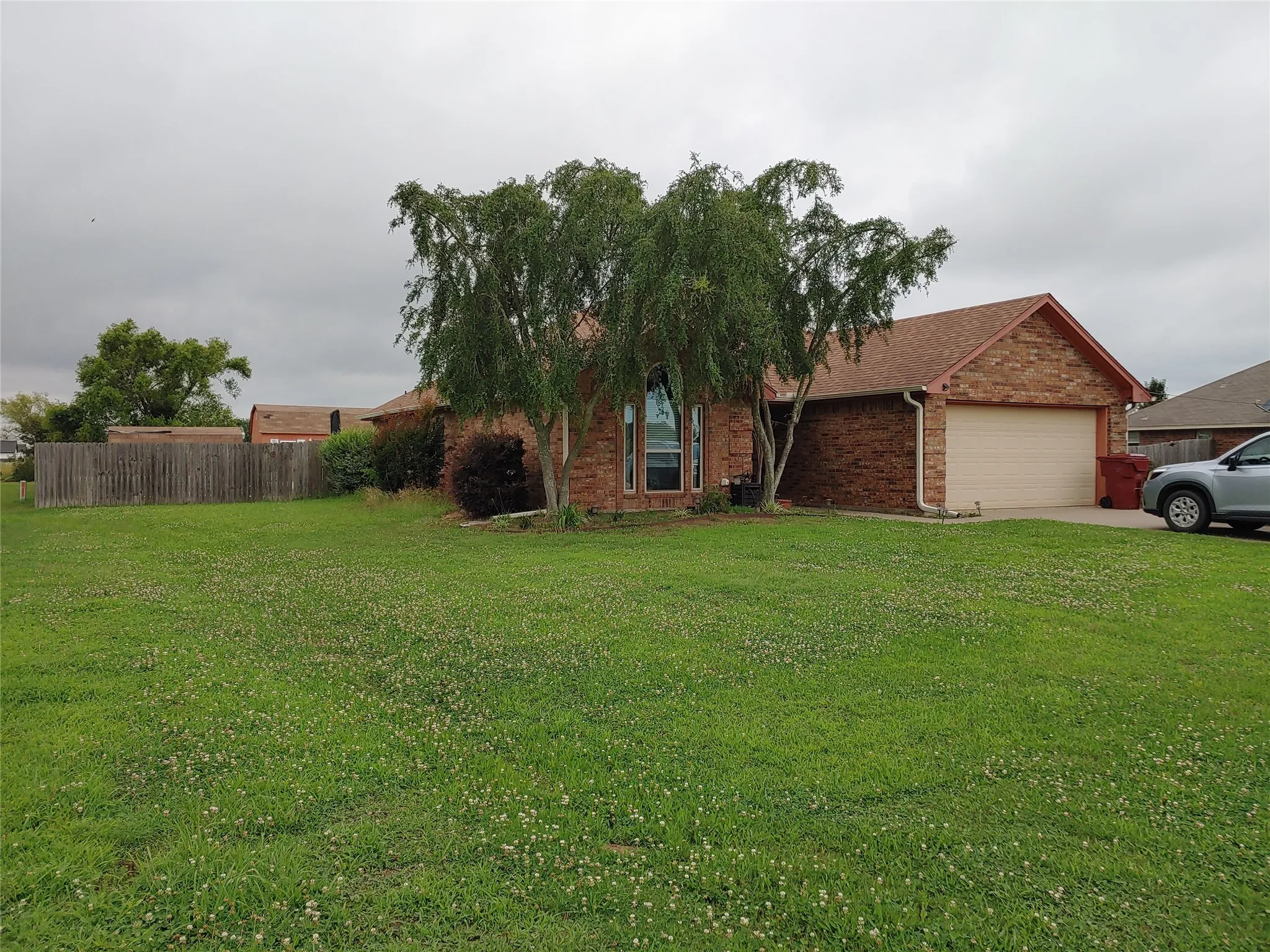 Brick exterior with a peaked roofline, an attached garage, and a large front lawn
