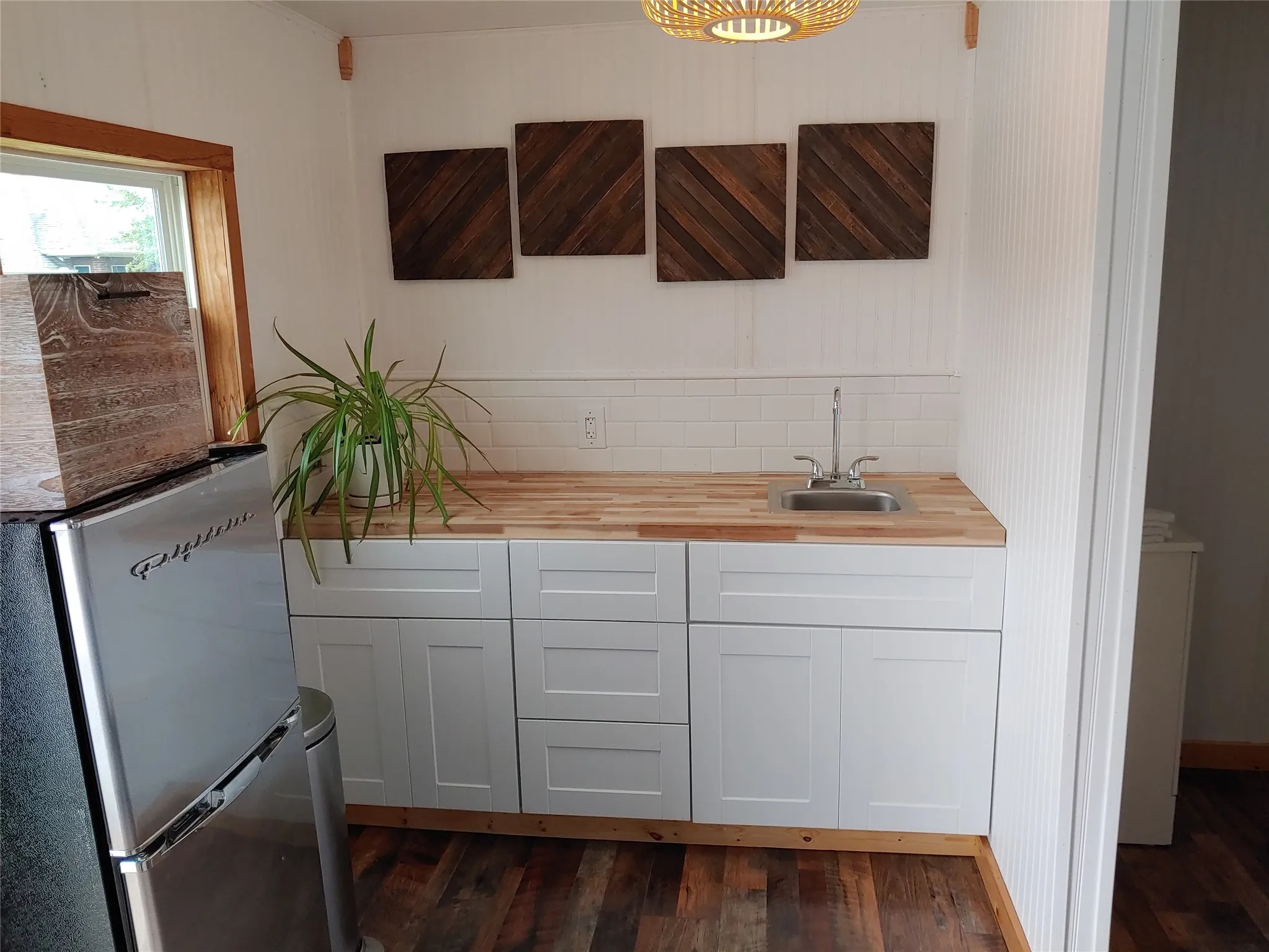 Compact wet bar featuring a stainless steel sink, wood-finish countertop, and white shaker-style cabinetry