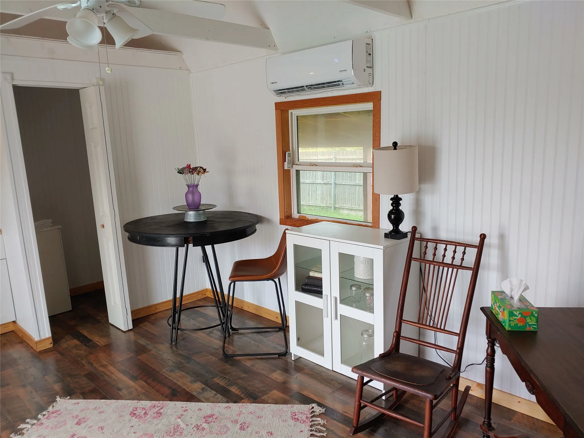 Interior space featuring wood-finish flooring, white beadboard walls, and natural wood trim around the window