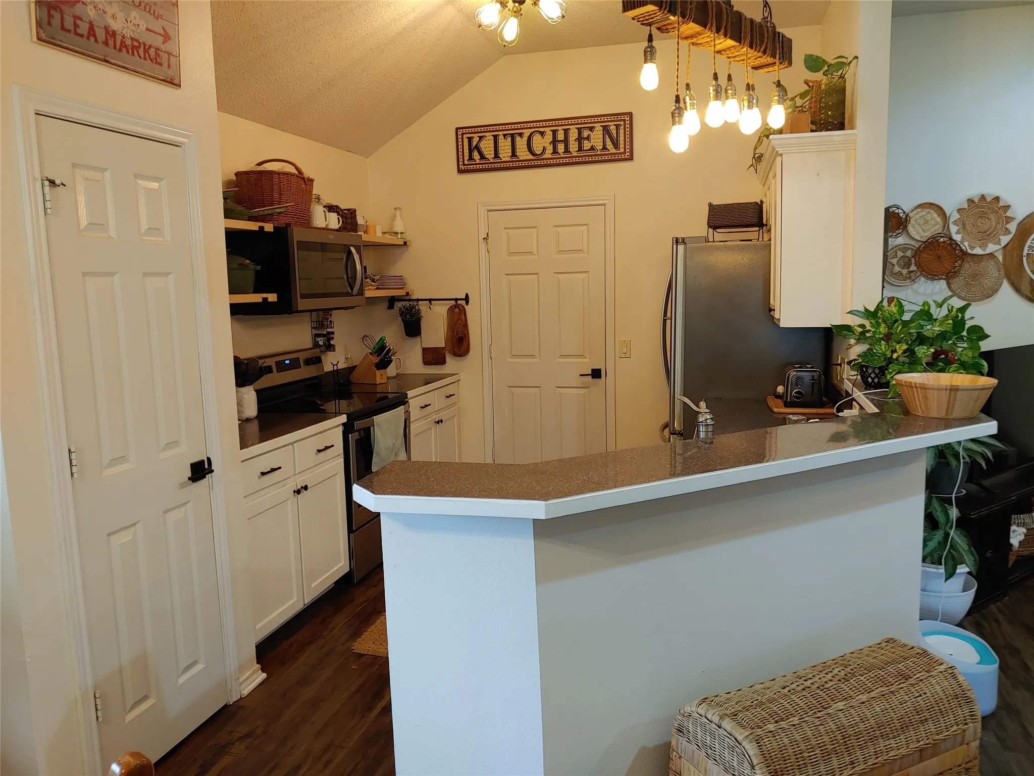 Kitchen featuring a vaulted ceiling, white cabinetry with dark hardware, dark countertops, and wood-finish flooring