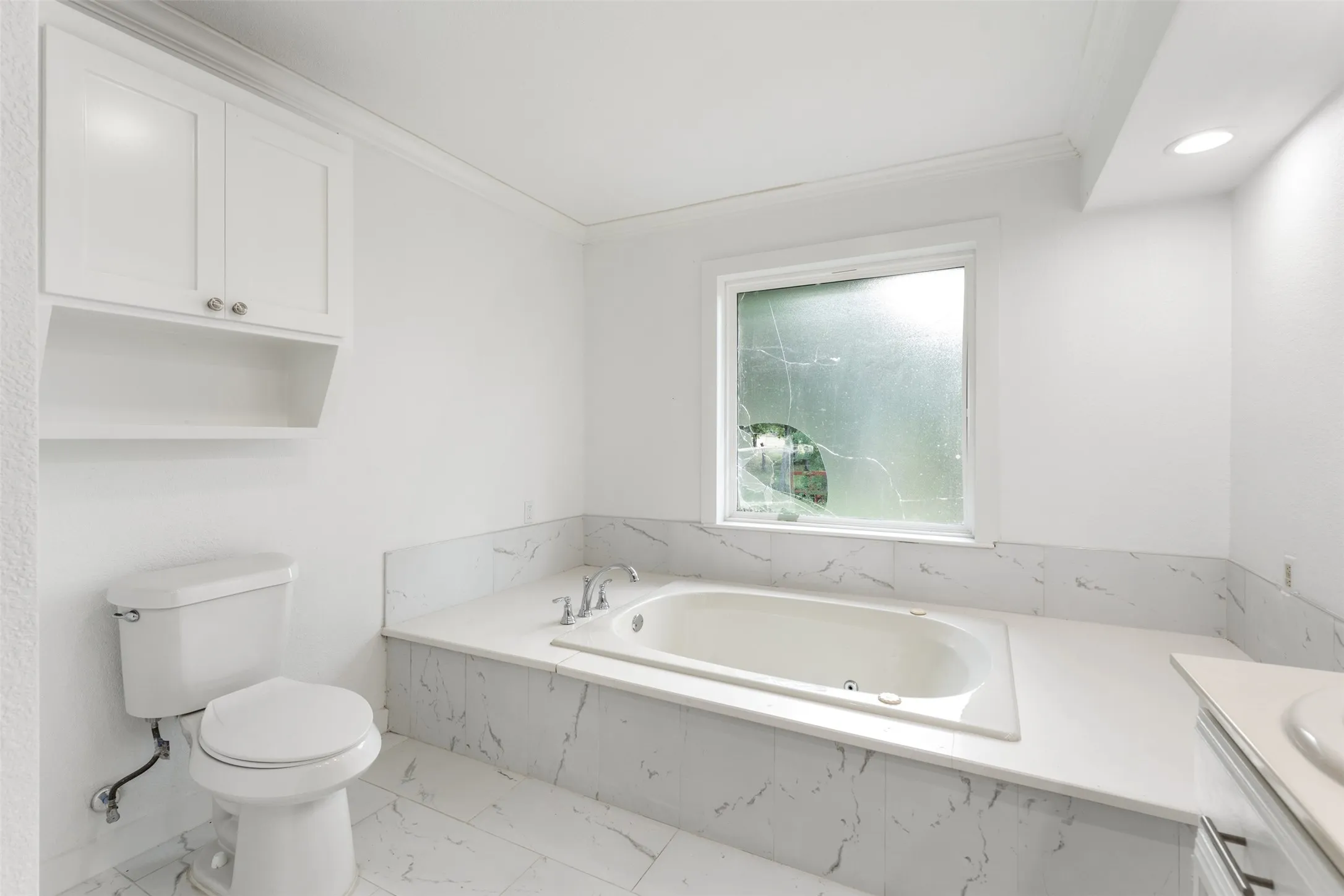 Bathroom featuring a built-in soaking tub, white wall cabinetry, and marble-look tile flooring