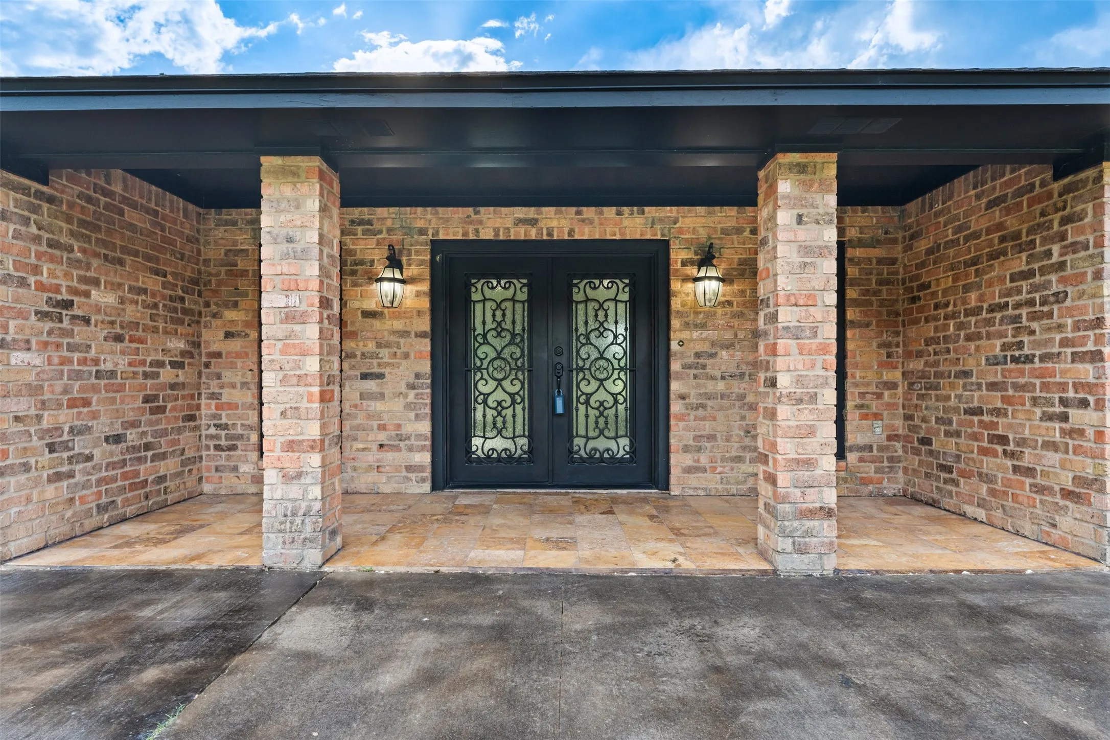 Brick exterior featuring a covered entry with dual sconces and an ornate double-door entry