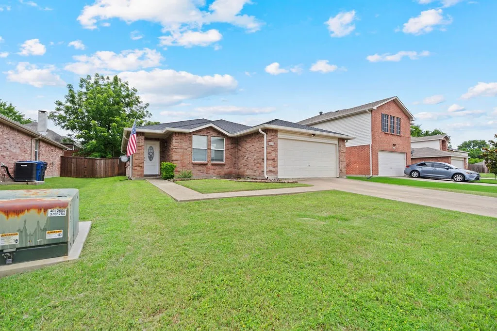 Brick exterior residence featuring a two-car garage, mature front lawn, and concrete driveway