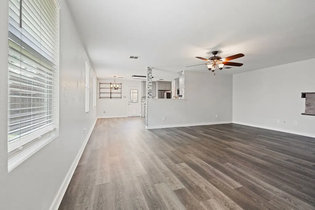 Spacious interior featuring wood-finish flooring, white walls, and multiple windows with blinds