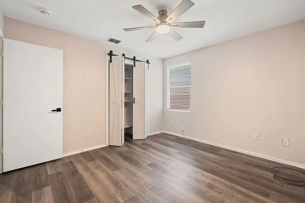 Bedroom featuring wood-finish flooring, a ceiling fan with integrated lighting, a window with blinds, and a closet with bi-fold barn doors