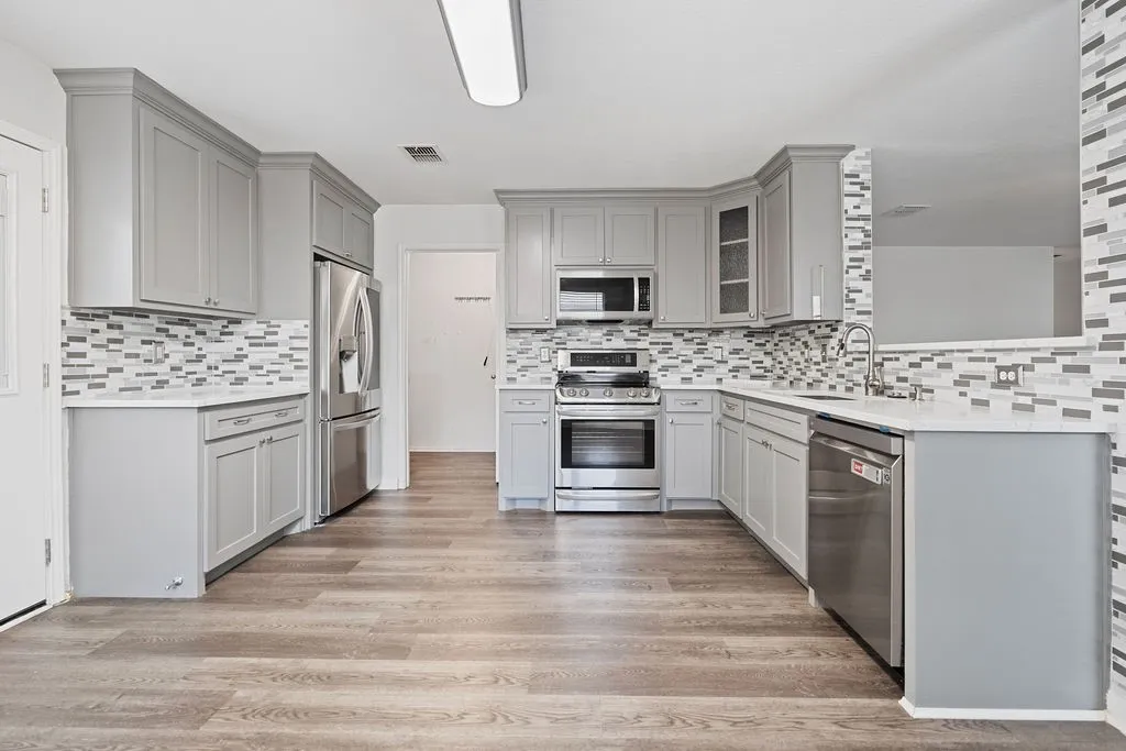 Kitchen featuring shaker-style cabinetry, stainless steel appliances, mosaic tile backsplash, wood-finish flooring, and solid surface countertops