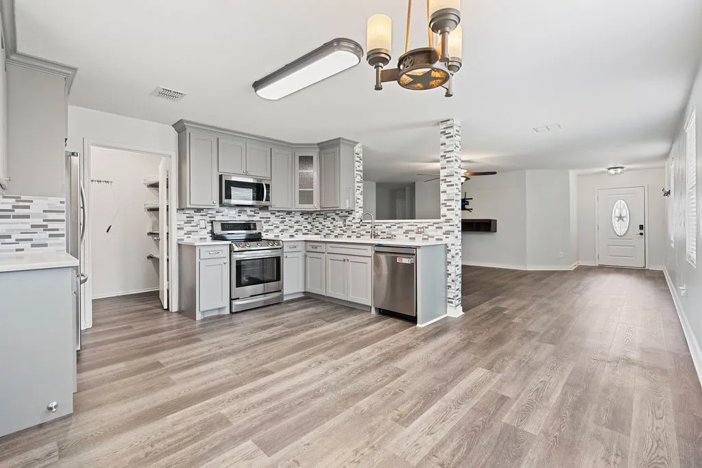 Contemporary kitchen with light gray cabinetry, stainless steel appliances, a multi-tone tile backsplash, and light-toned wood-finish flooring