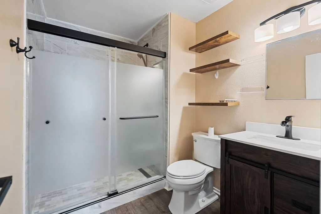 Bathroom featuring a frosted glass shower enclosure with dark framing, a dark wood-finish vanity with a white countertop and integrated sink, a dark bronze-finish faucet, and coordinating wall-mounted light fixture
