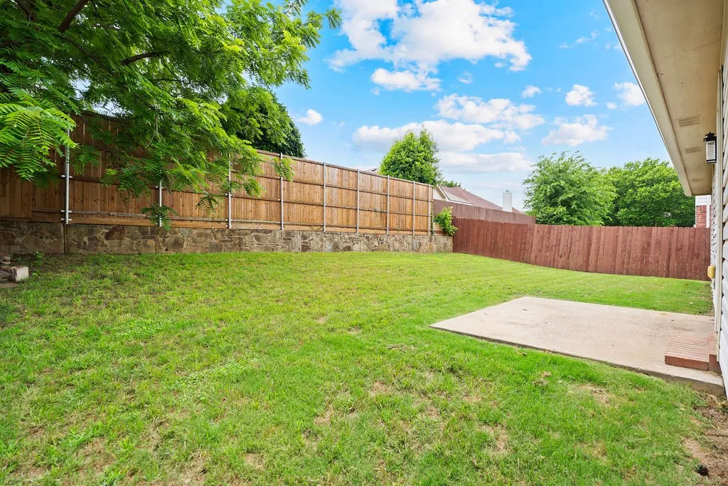 Spacious backyard featuring a concrete patio, mature tree, and a combination of wood and stone fencing